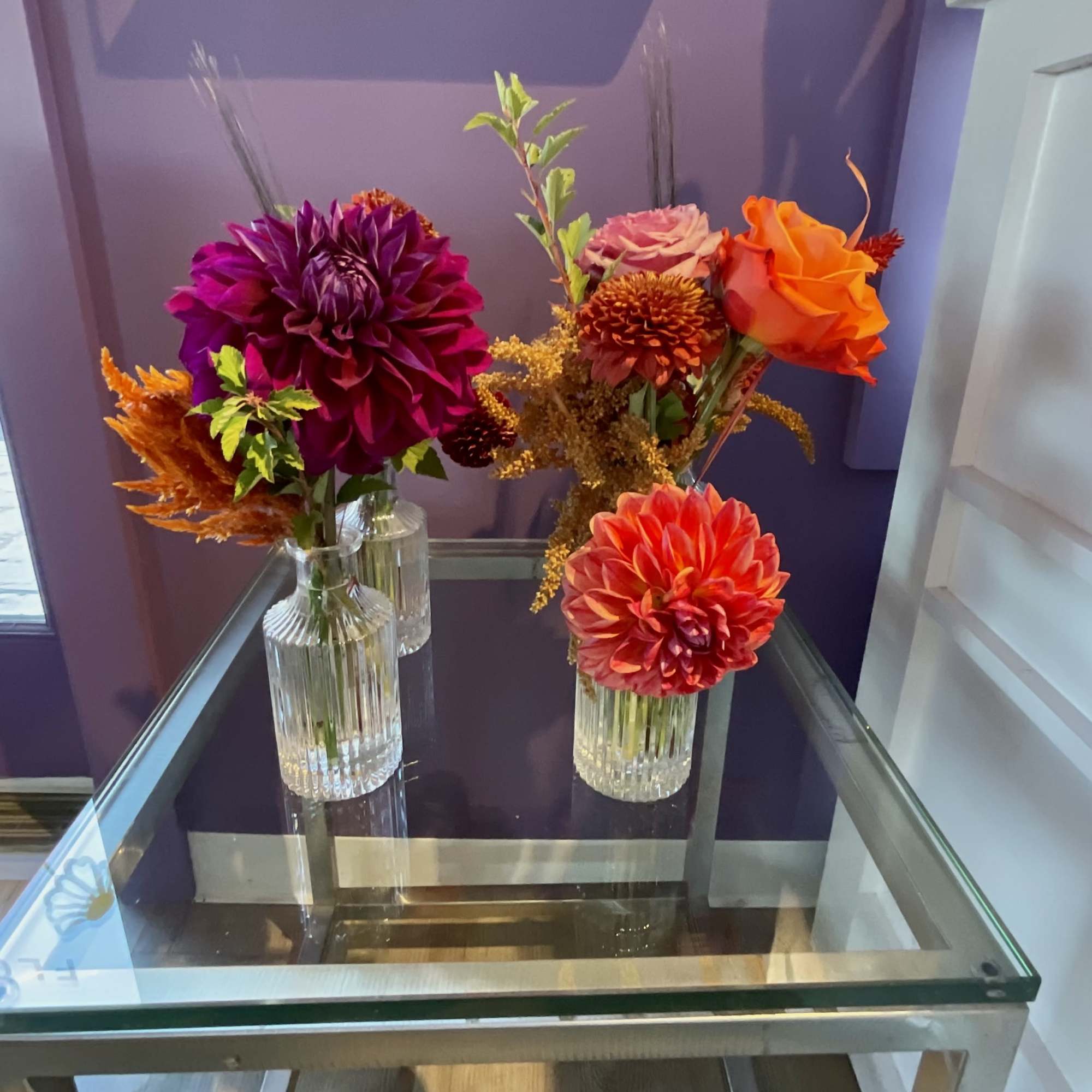 Three small floral arrangements in clear glass vases on a glass table