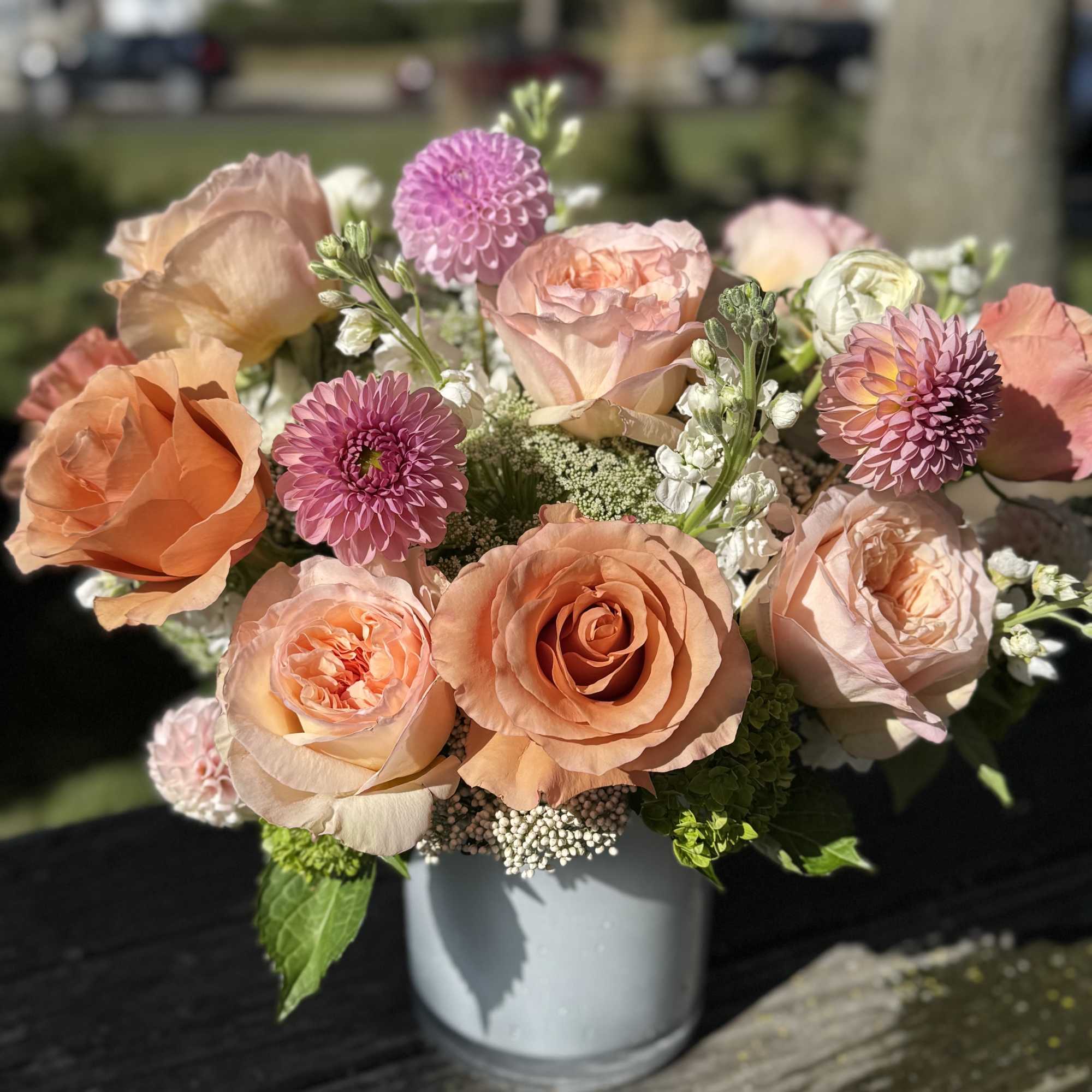 Peach and pink roses with purple blooms in a gray vase