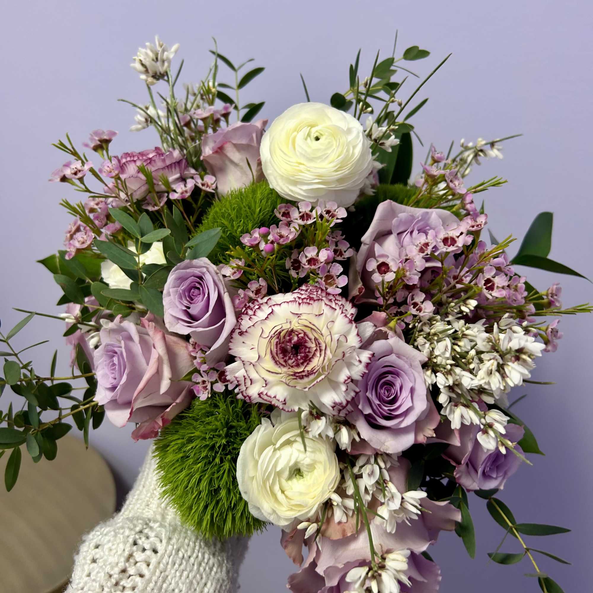 Handheld bouquet of lavender roses and white blooms with greenery