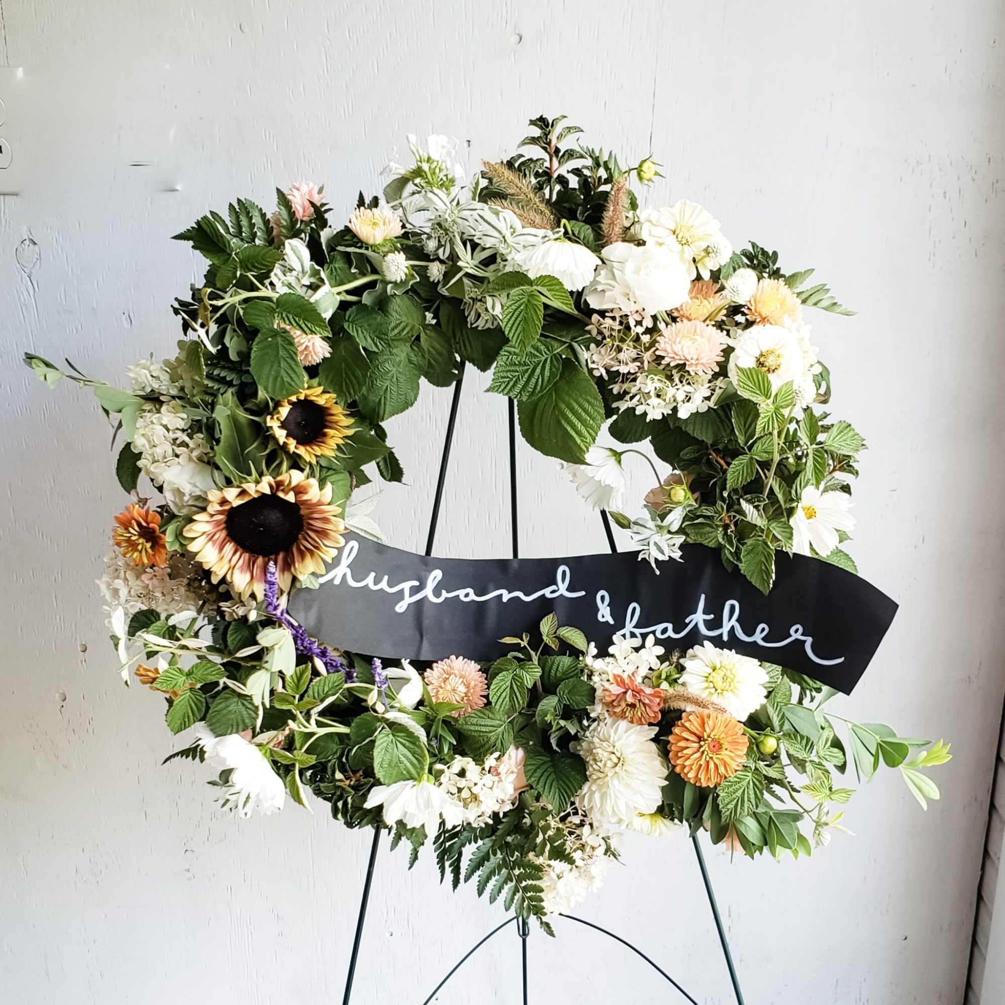 Floral wreath on an easel with a black ribbon reading husband & father