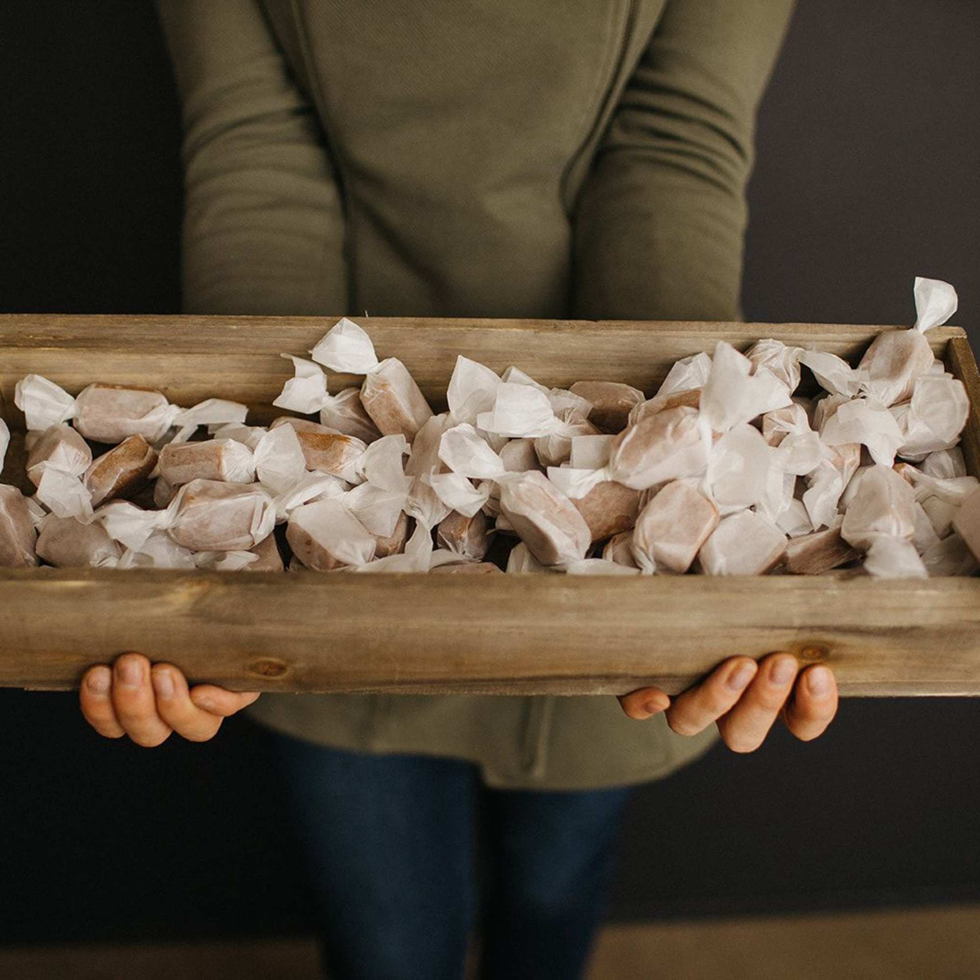 Wooden tray filled with wrapped candies held by a person