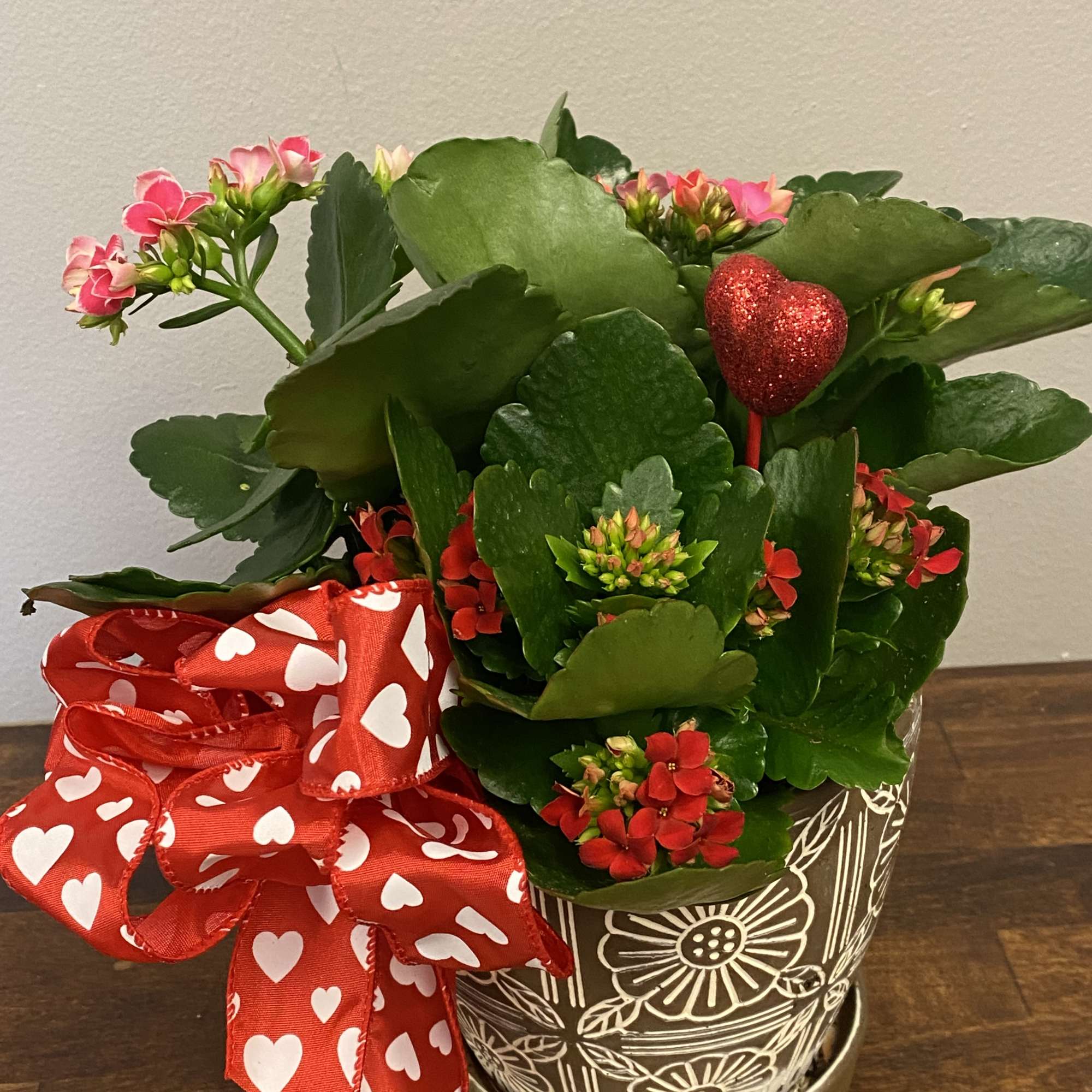 Potted flowering plant with pink and red blooms, a heart pick, and a red heart ribbon
