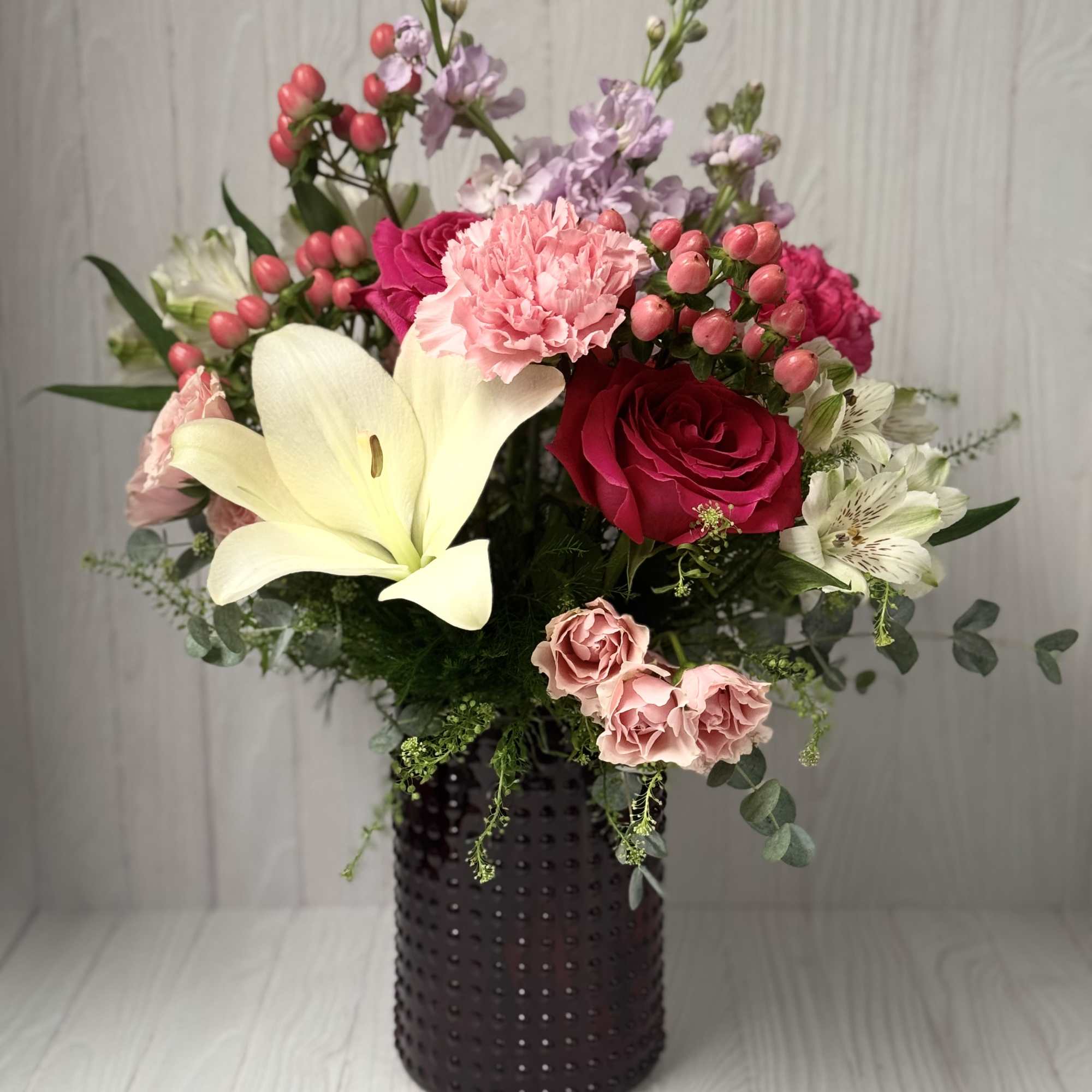 Mixed bouquet with roses, lilies, and carnations in a dark vase