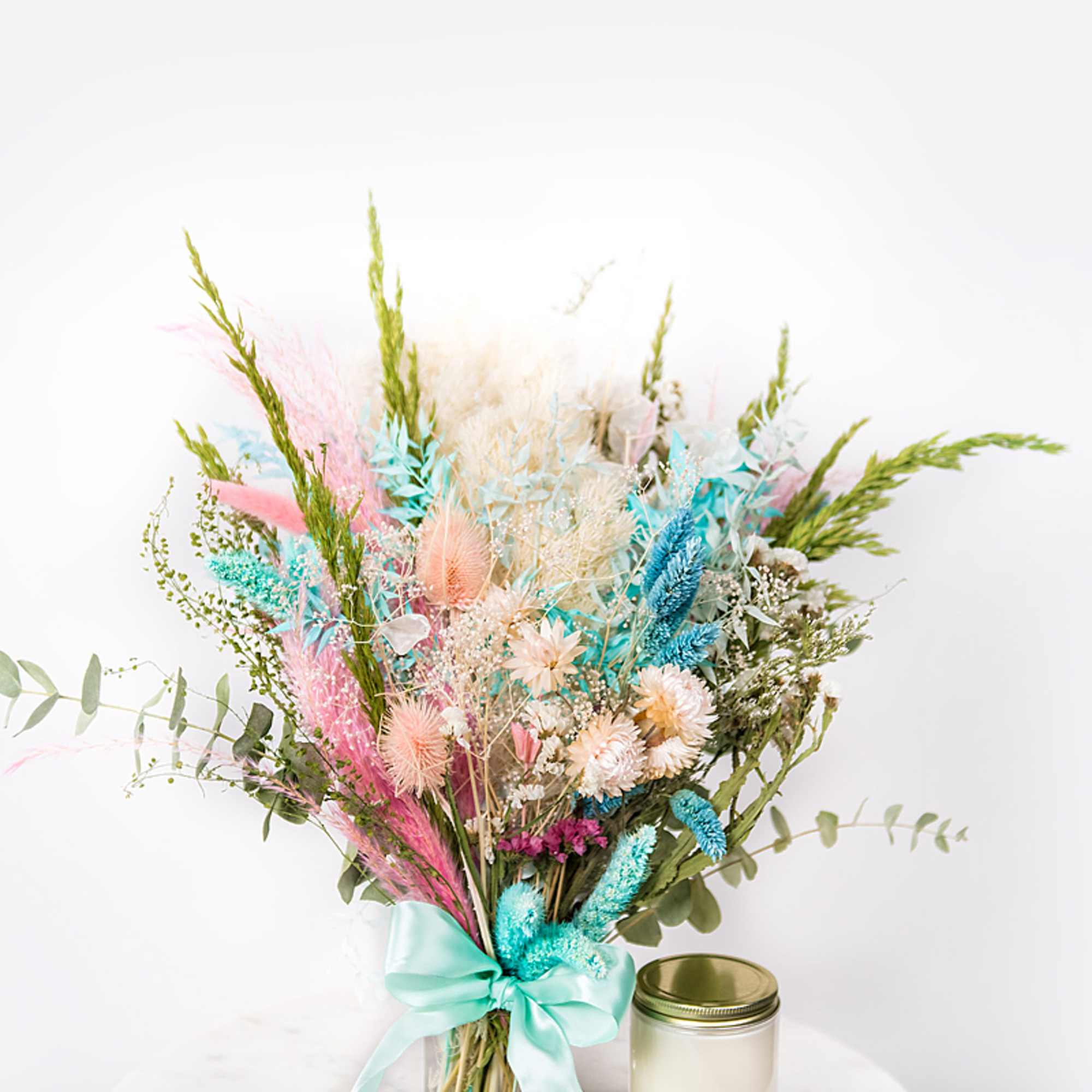 Pastel dried flower bouquet tied with a satin ribbon beside a candle jar