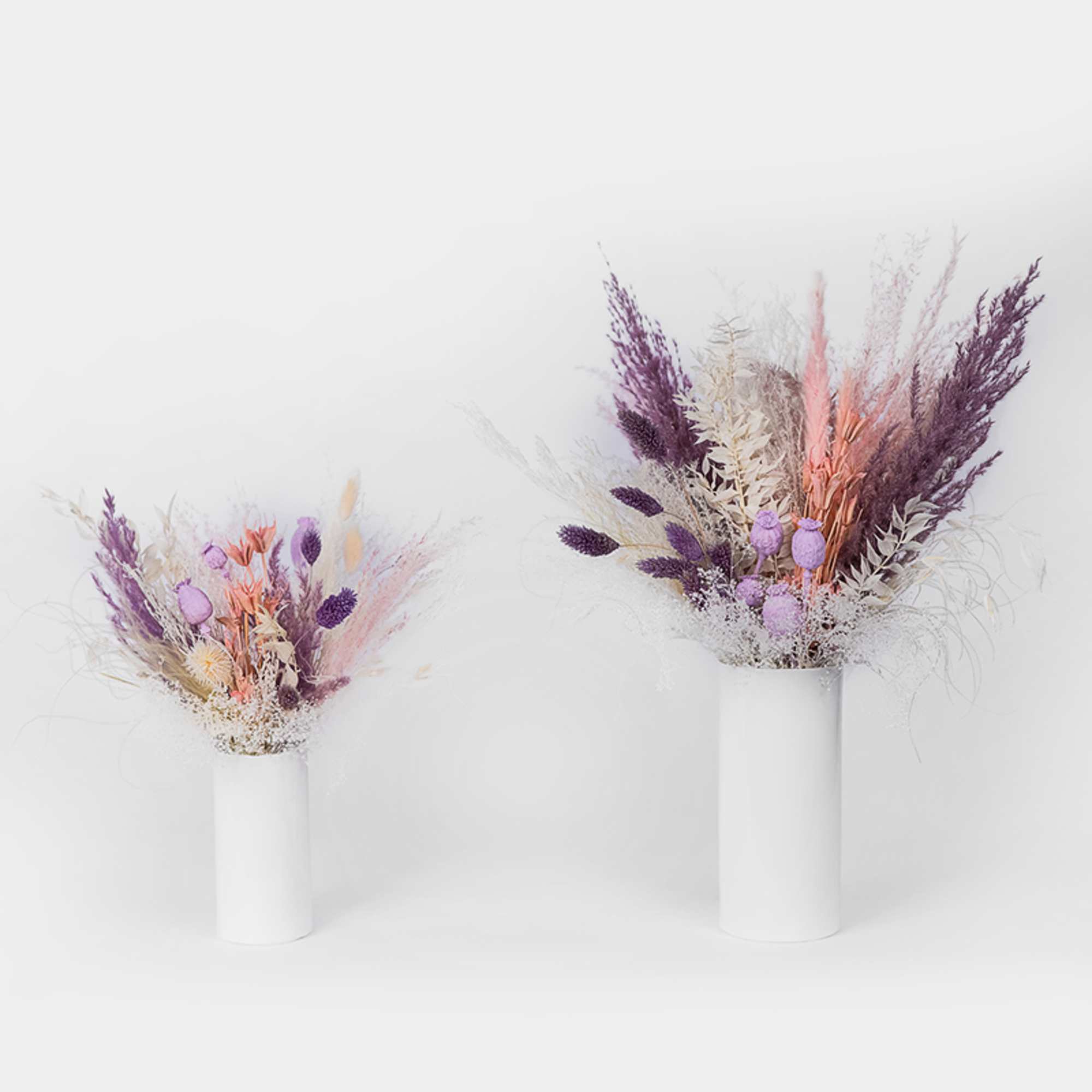 Two dried floral arrangements in white vases with purple and peach accents