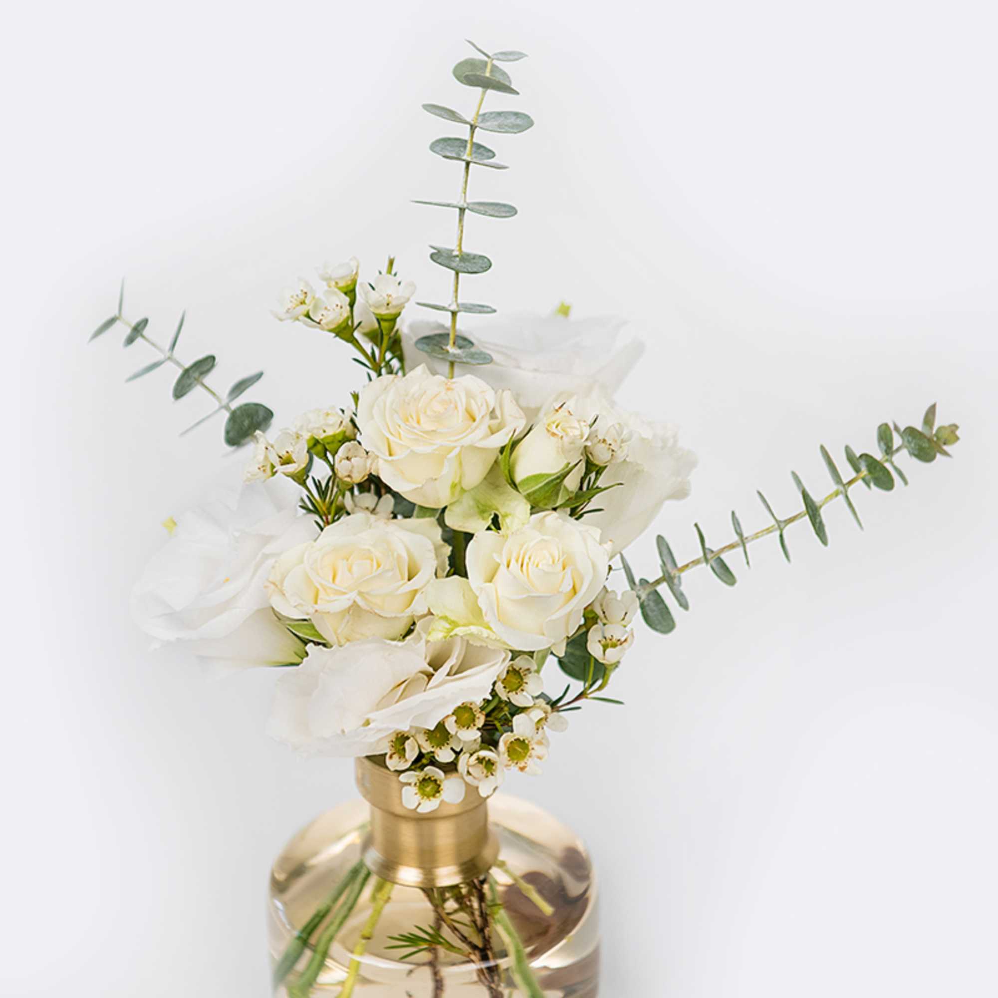 White roses and small white blooms in a gold vase with eucalyptus stems