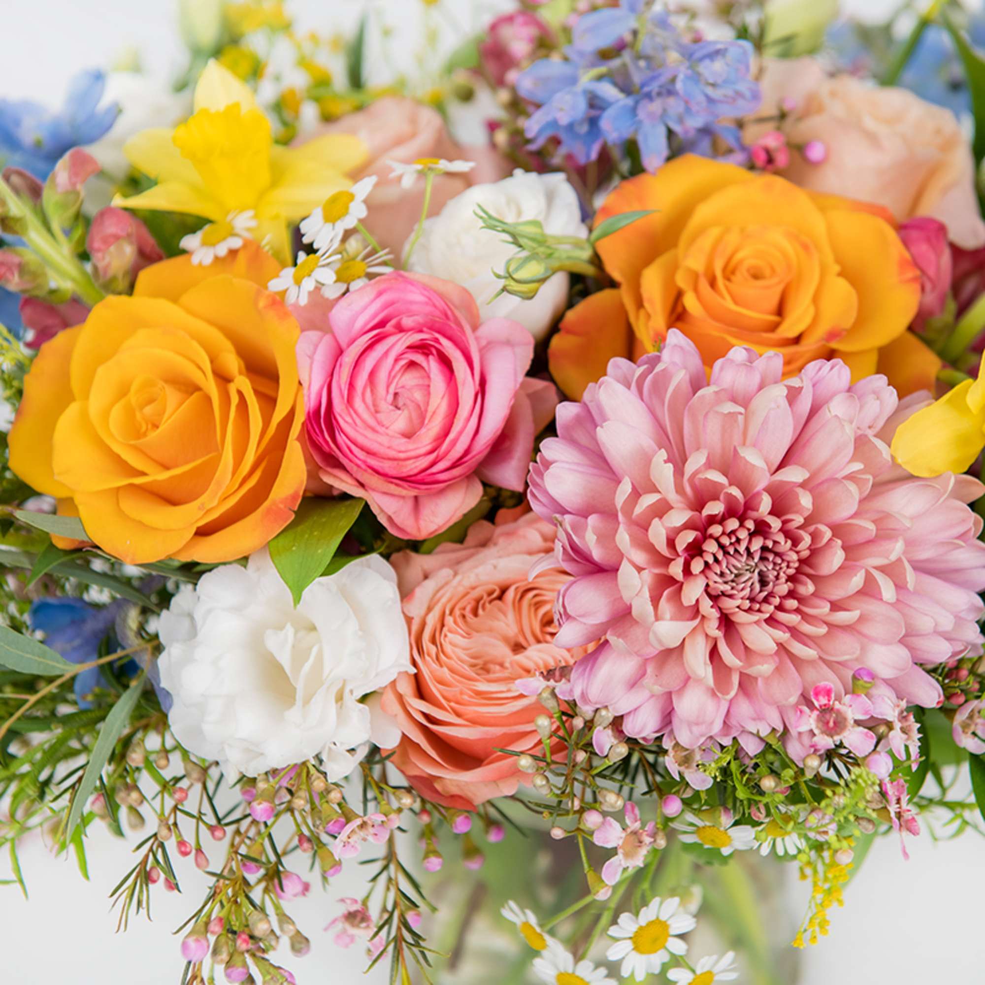 Colorful bouquet with orange roses, pink blooms, yellow daffodils and a large pink chrysanthemum in a glass vase.