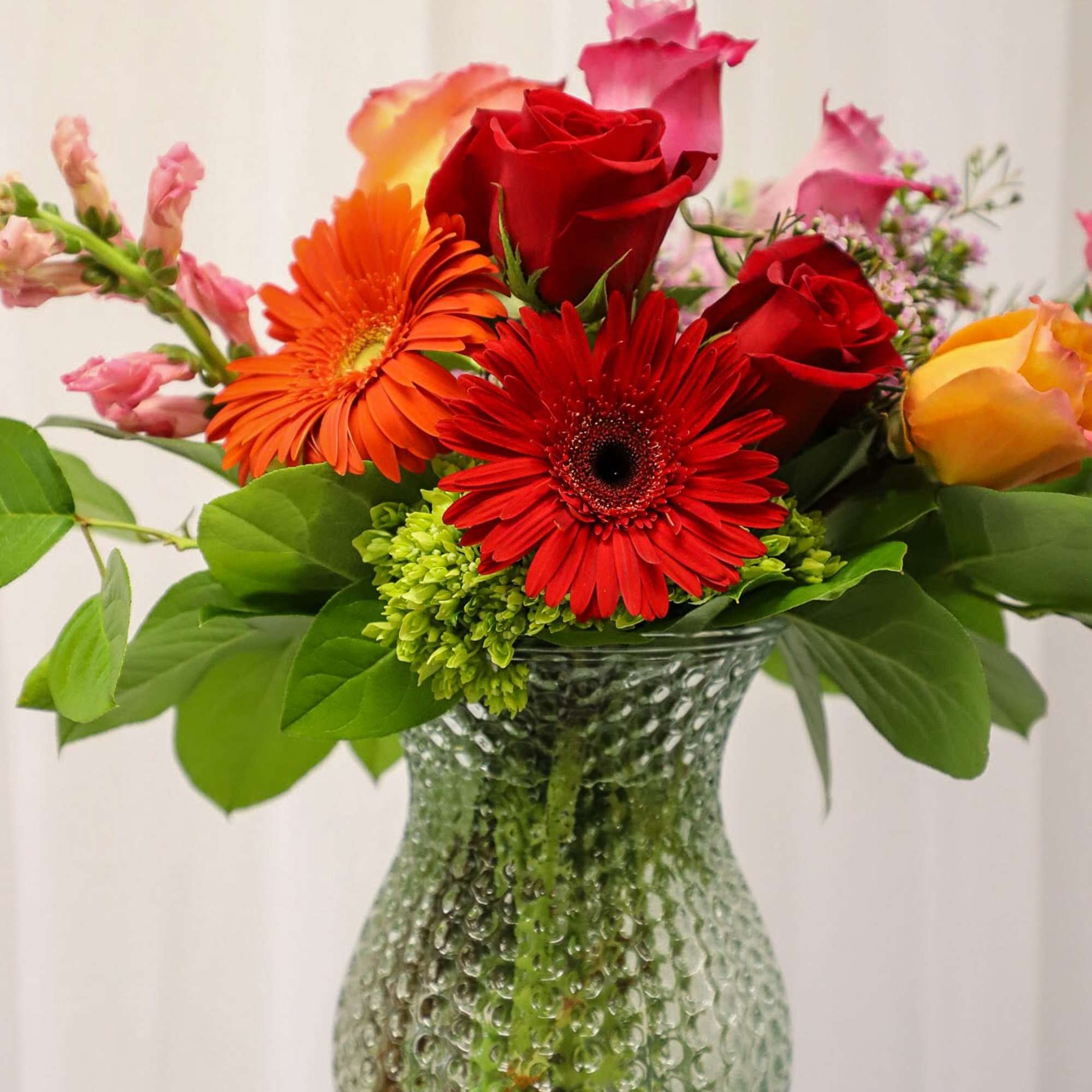 Mixed bouquet of red roses and gerbera daisies in a textured glass vase