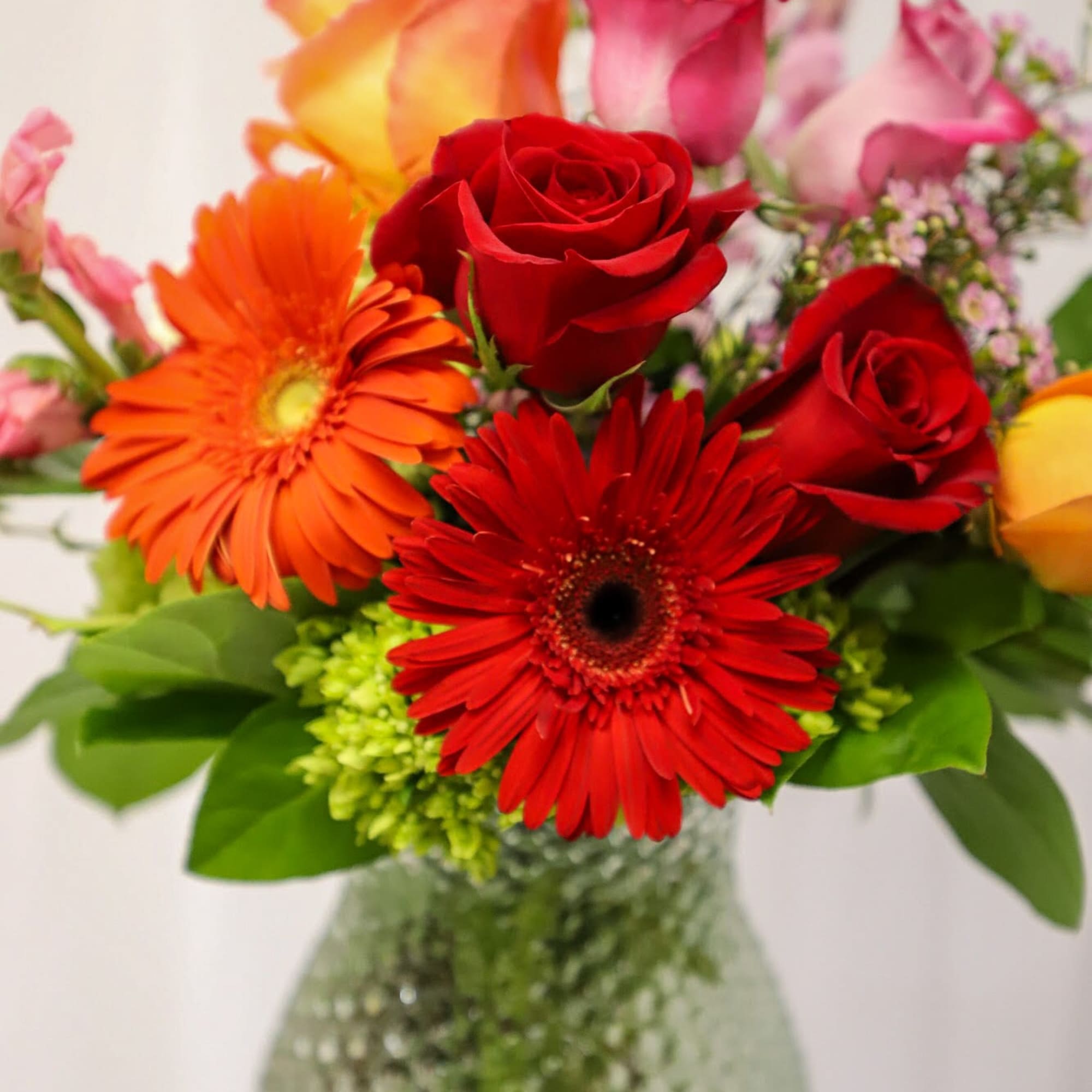 Mixed bouquet of red roses and orange gerbera daisies in a glass vase