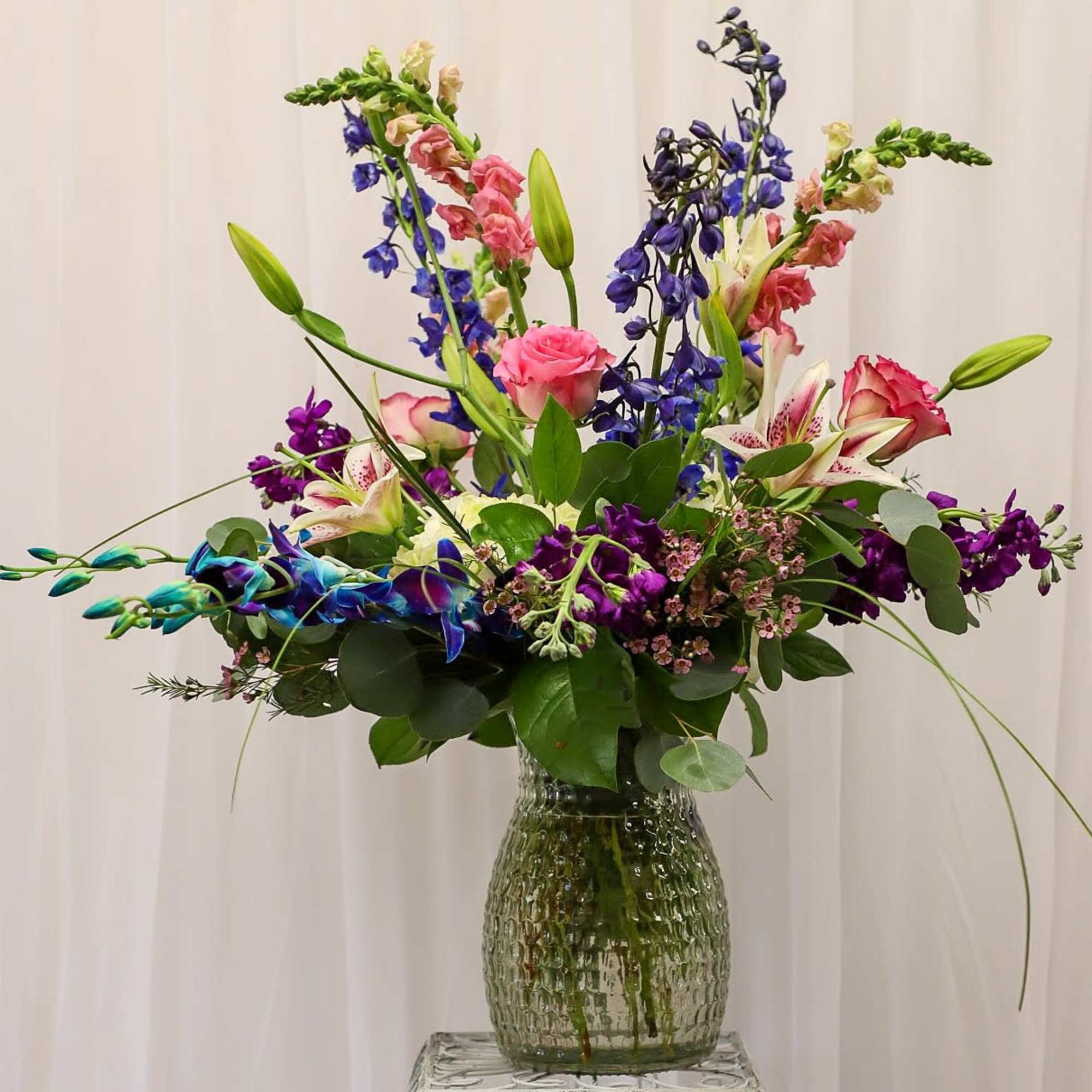 Tall mixed bouquet with lilies, roses, and purple blooms in a glass vase