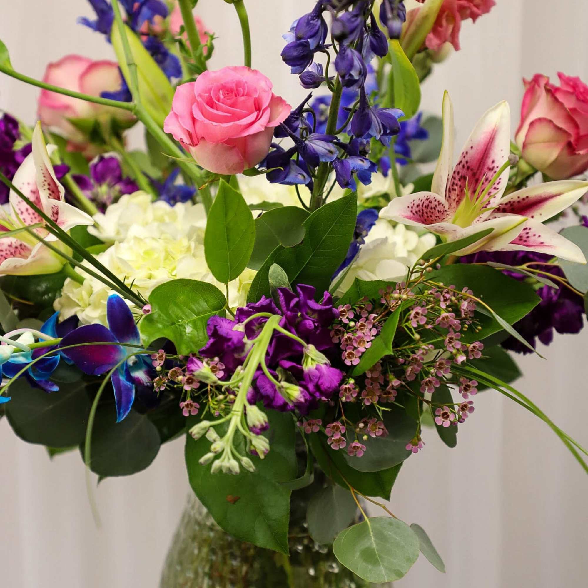 Mixed bouquet with pink roses, lilies, and purple flowers in a glass vase