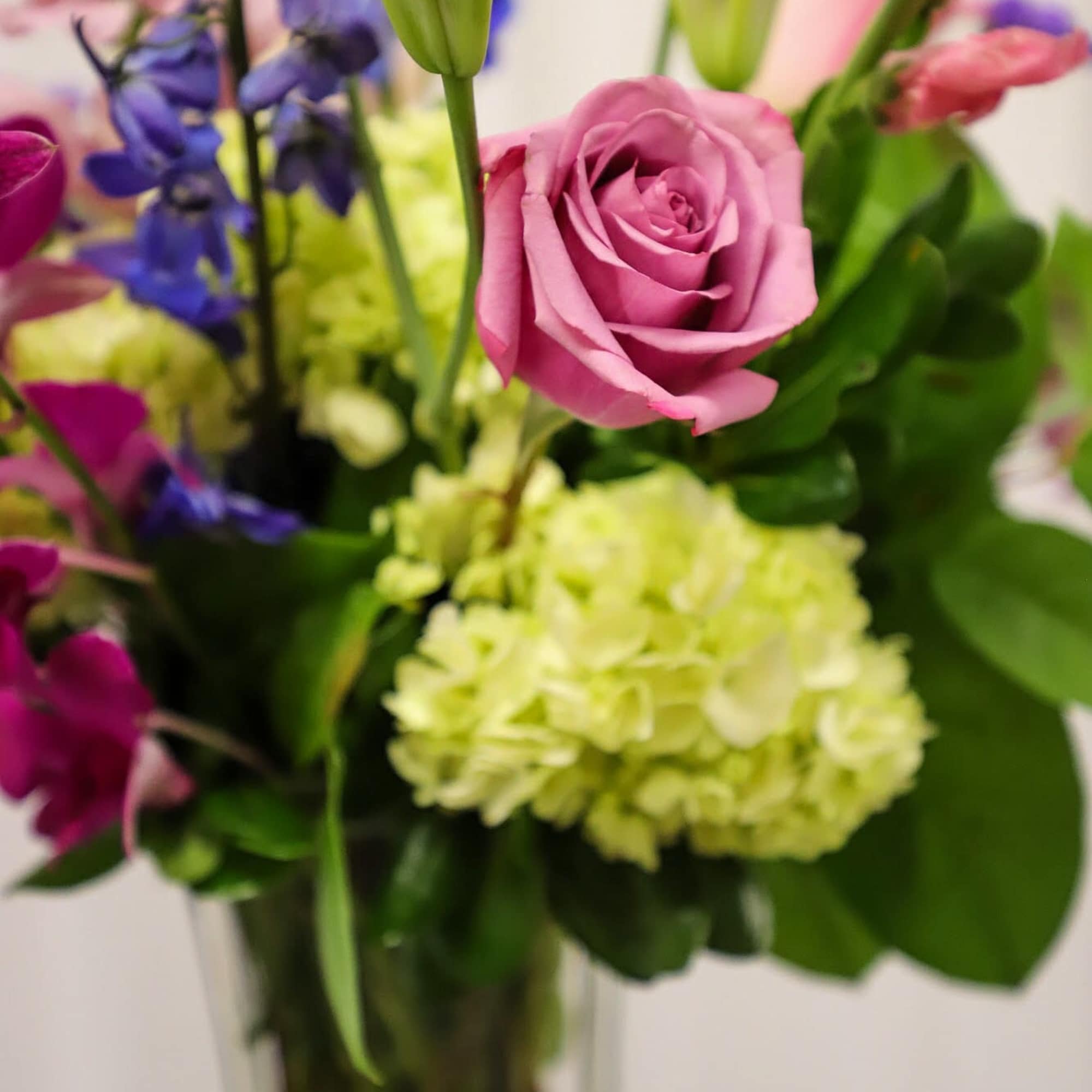 Mixed bouquet with a pink rose, green hydrangea, and purple flowers in a vase