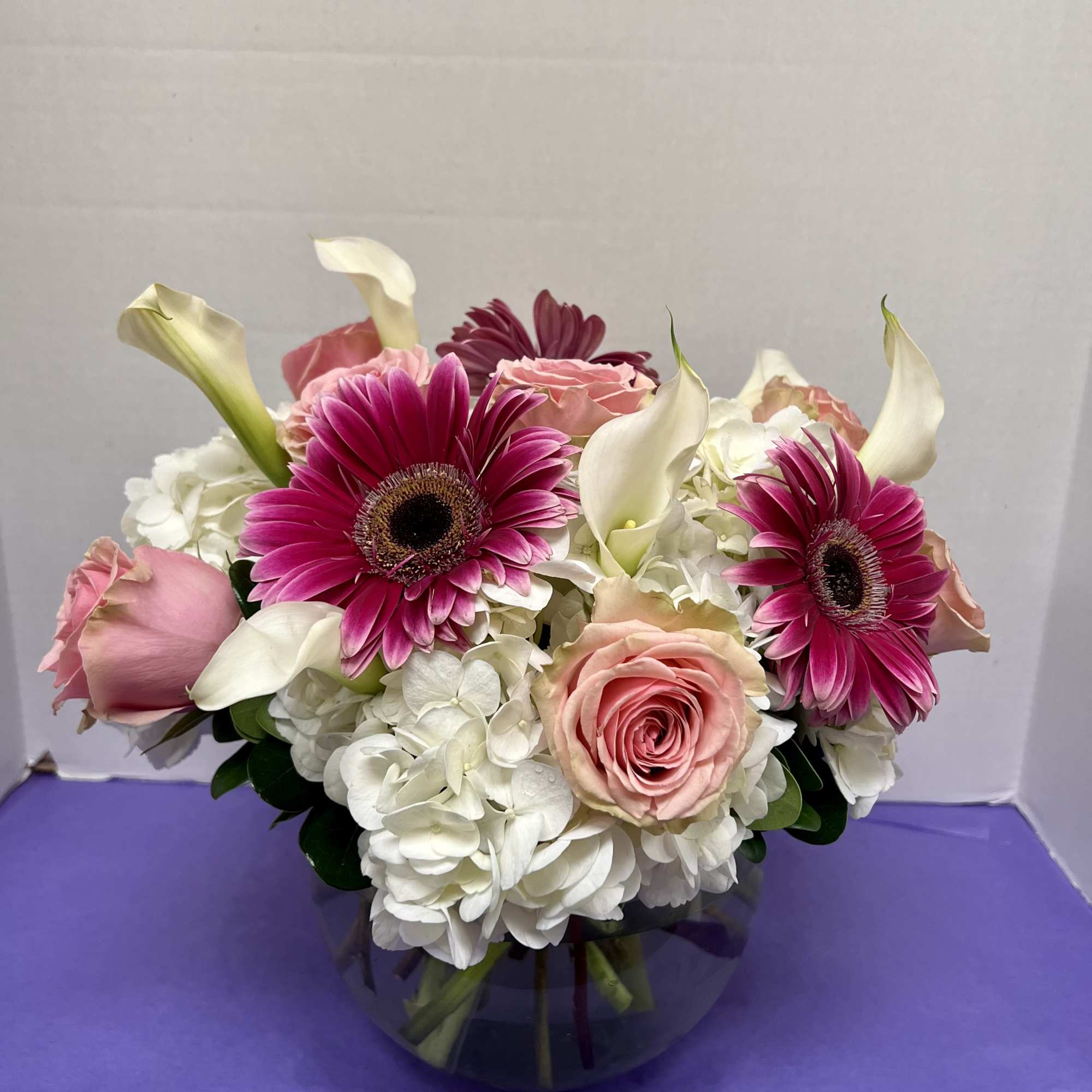 Pink gerberas, roses, white hydrangeas, and calla lilies in a glass vase