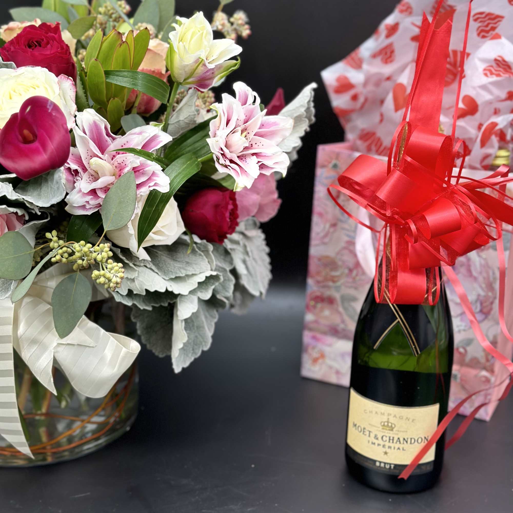 Bouquet of pink and white flowers beside a champagne bottle with a red ribbon