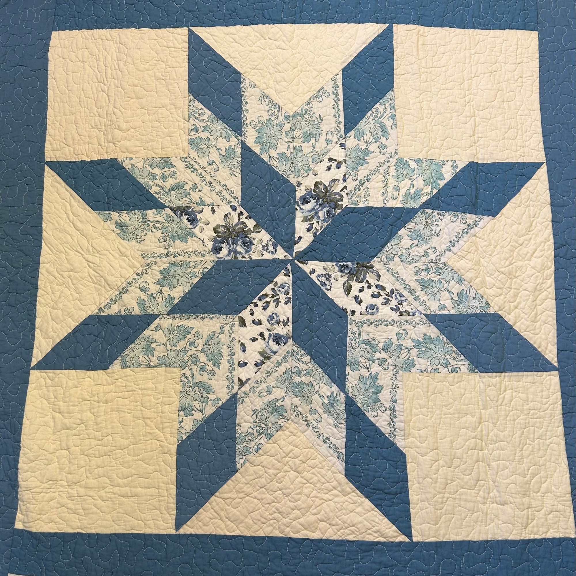 Blue and cream quilt with a star pattern and floral fabric accents