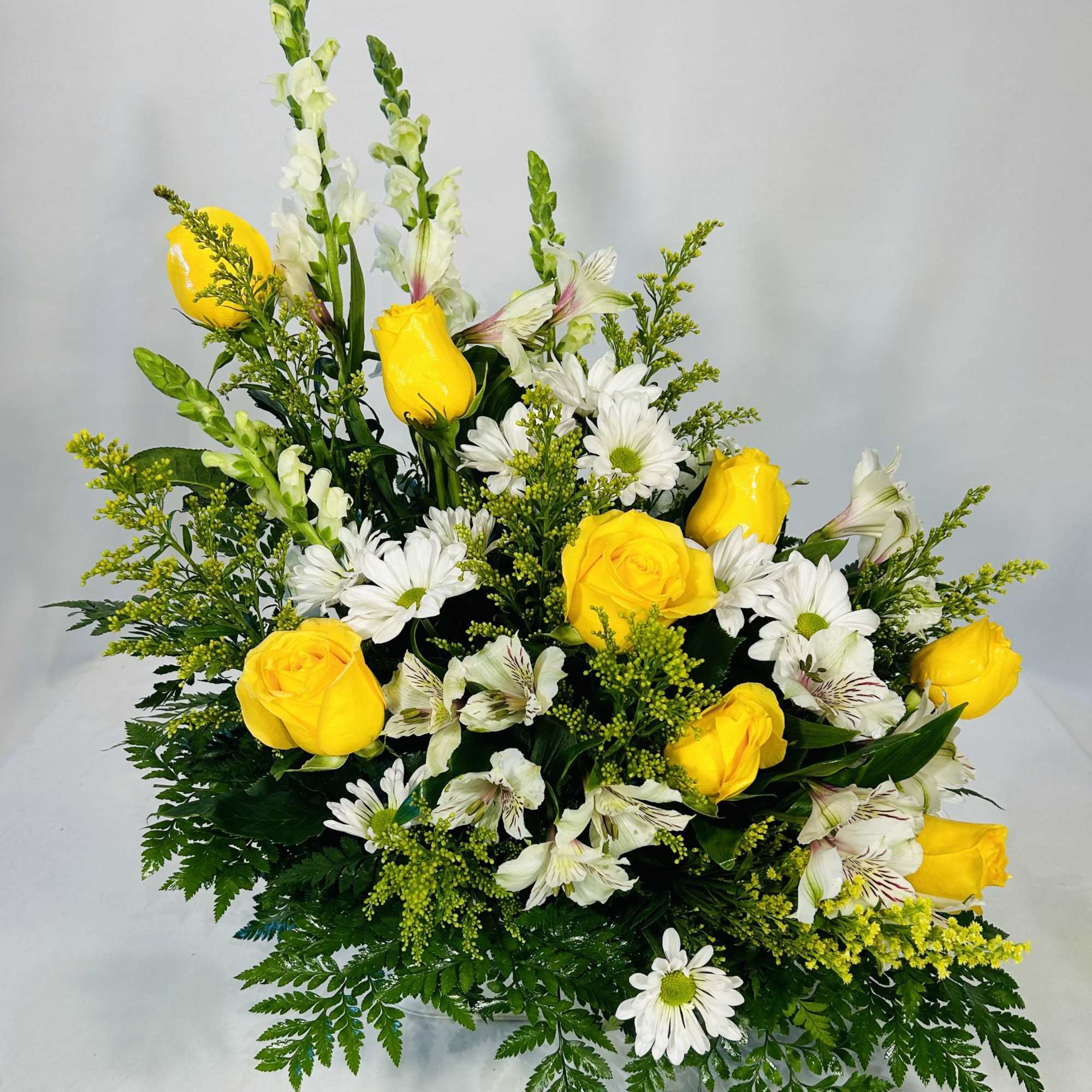 This yellow and white arrangement features yellow roses and white snapdragons accented