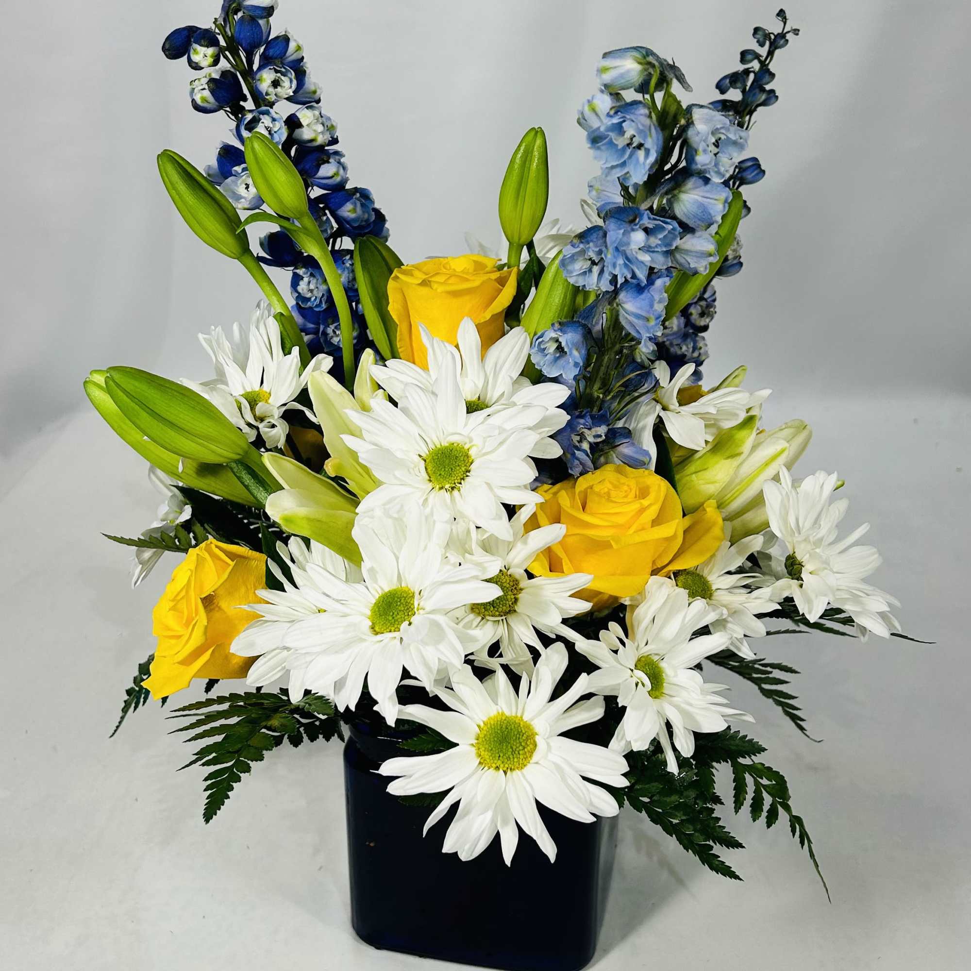 Yellow roses and white daisies in a black vase with blue flowers
