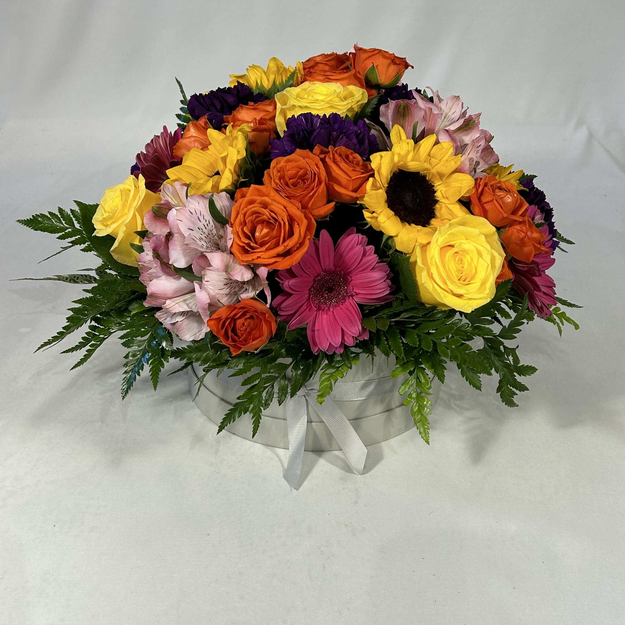 Bright, cheerful blooms spill from a round white hat box tied with