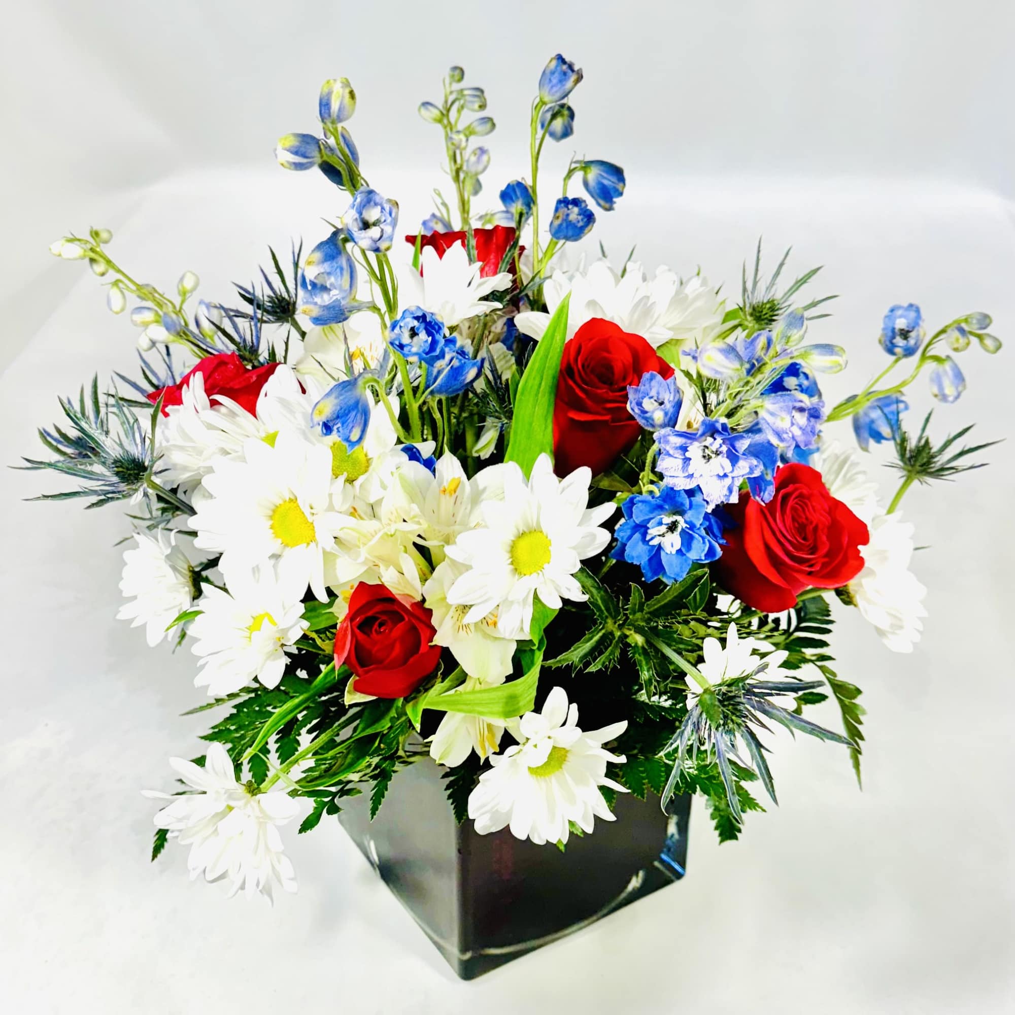 Red roses, white daisies, and blue flowers in a black vase