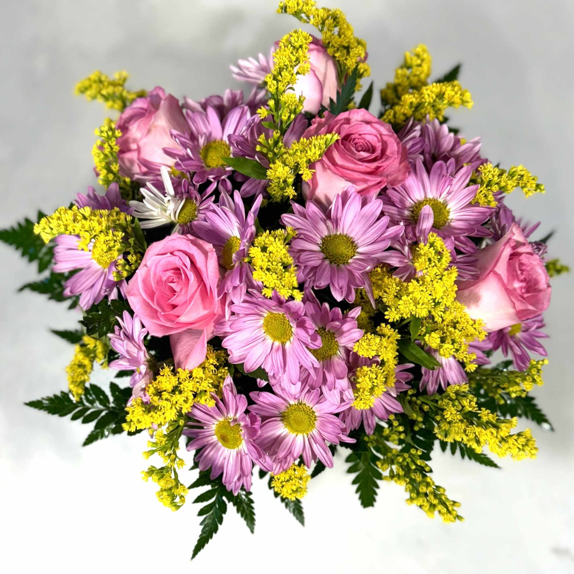 Pink roses and purple daisies with yellow filler flowers in a bouquet