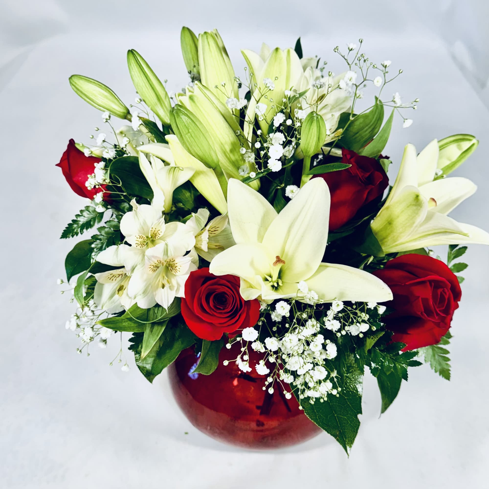 Bouquet of white lilies and red roses in a red glass vase