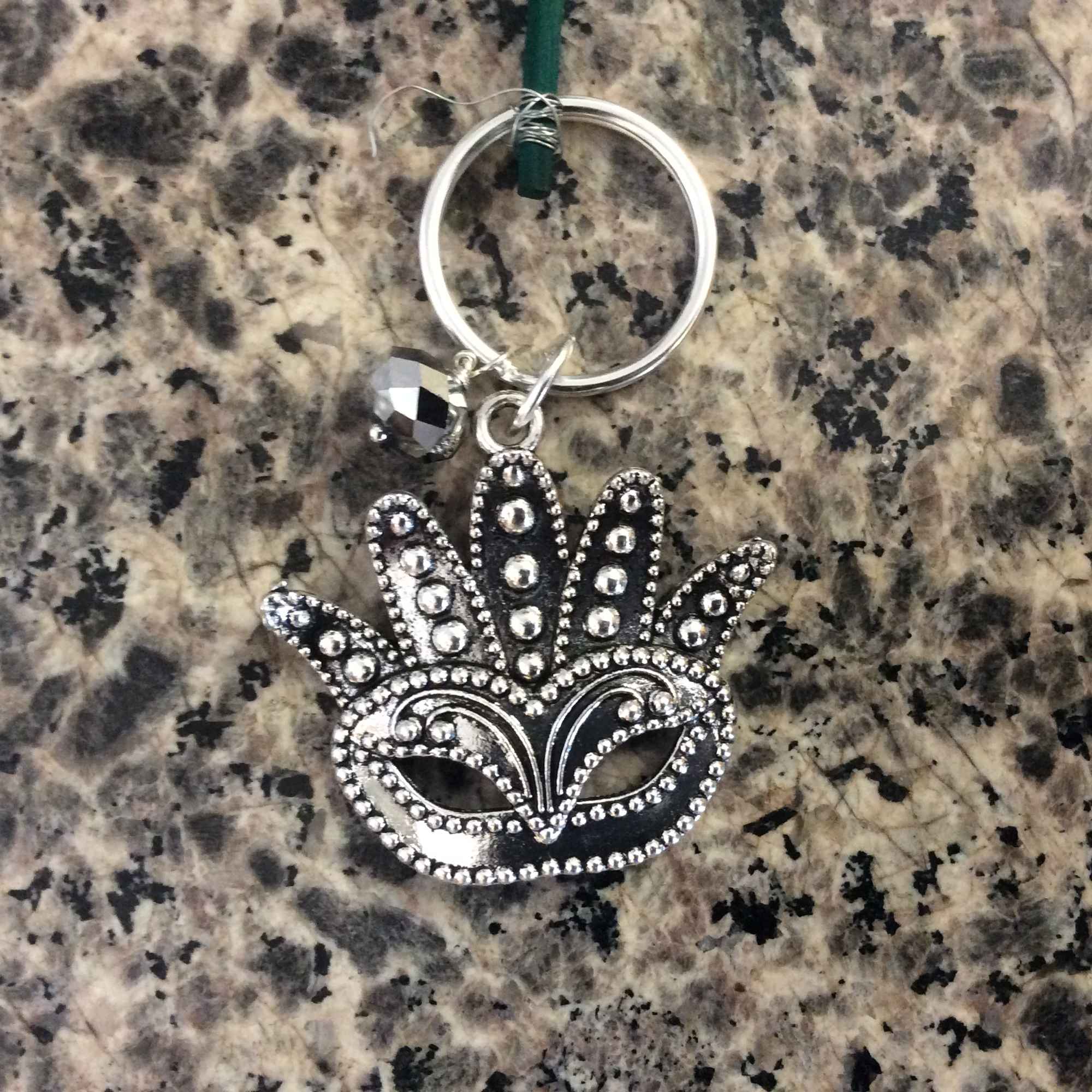 Silver keychain with a beaded mask charm on a granite surface