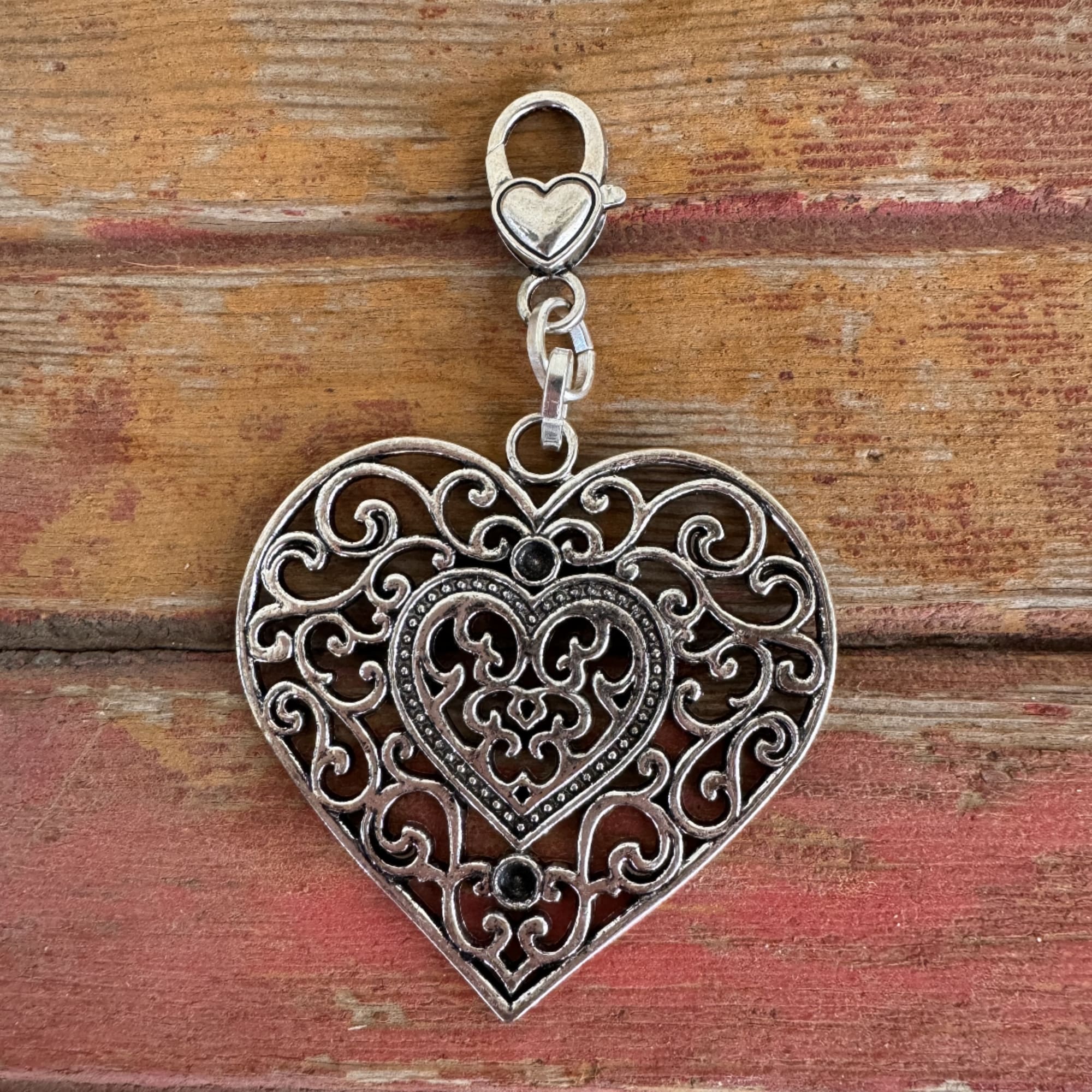 Silver heart-shaped filigree charm on a wooden surface