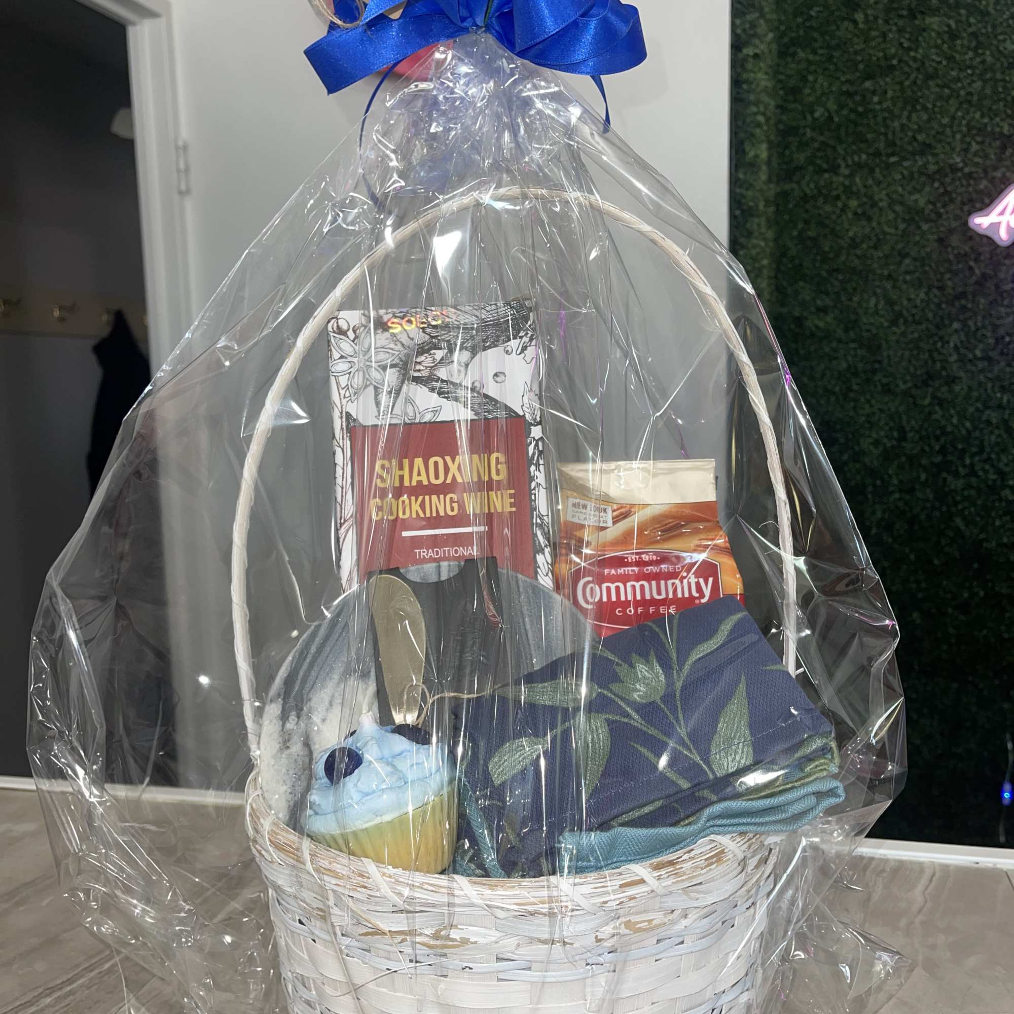 Gift basket with cooking wine, coffee, a cupcake, and folded cloths wrapped in clear plastic