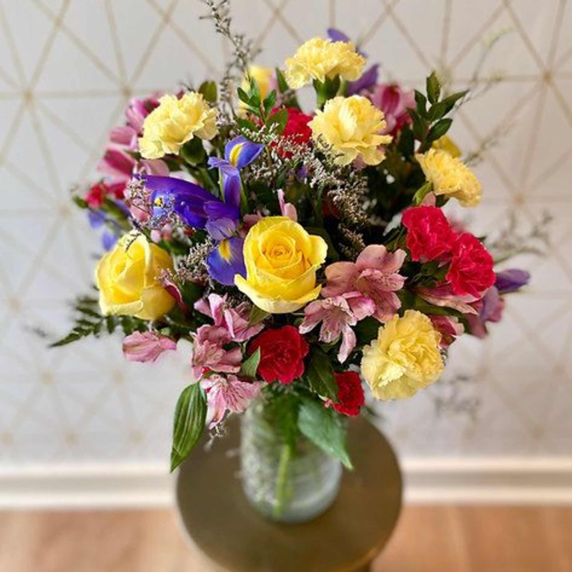Mixed bouquet of roses, carnations, and purple flowers in a glass vase