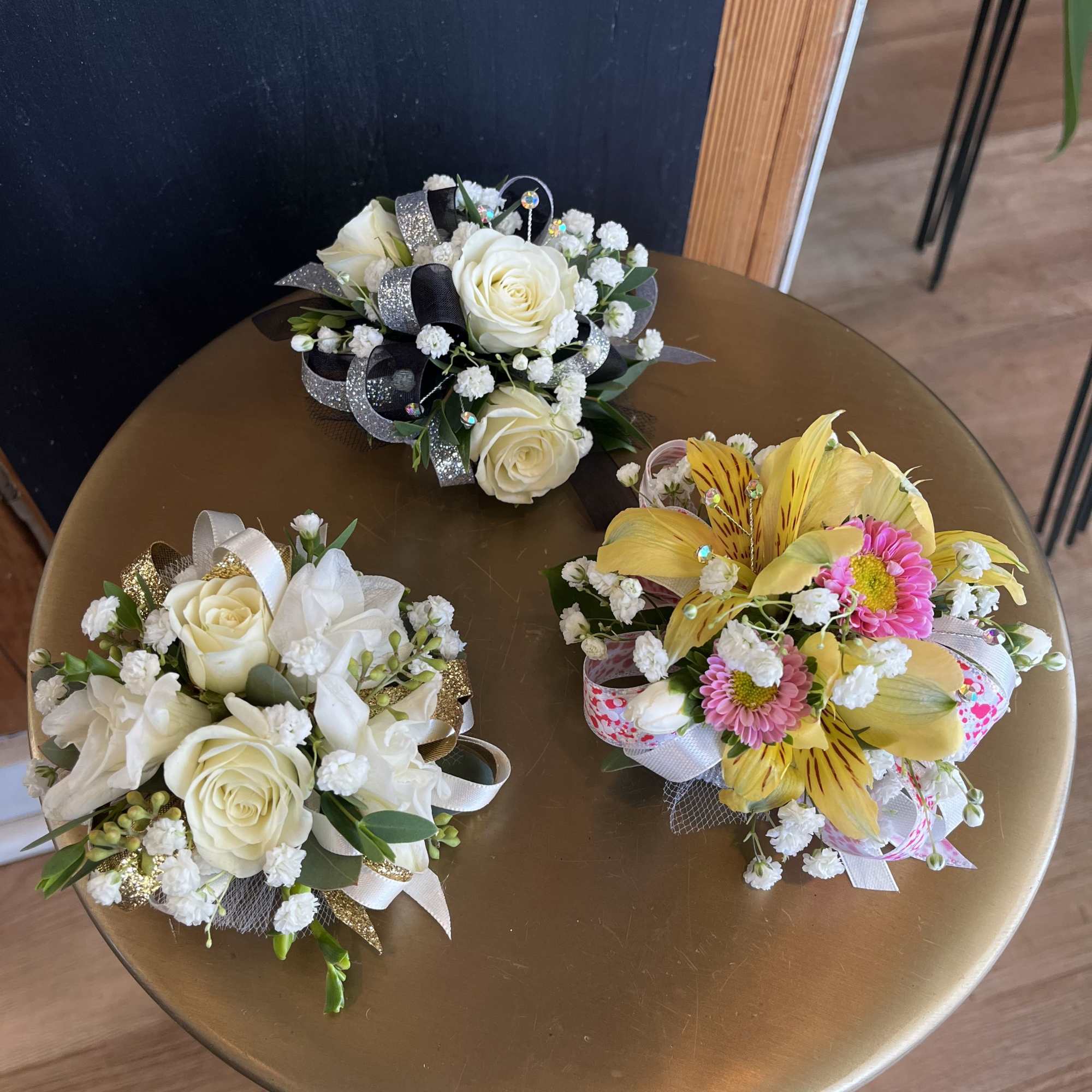 Three small floral bouquets with white roses and yellow blooms on a round table.