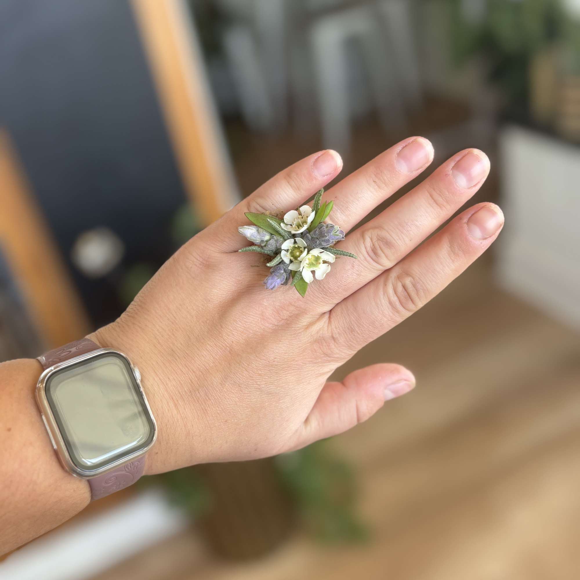 Hand wearing a small floral ring with white and lavender blossoms