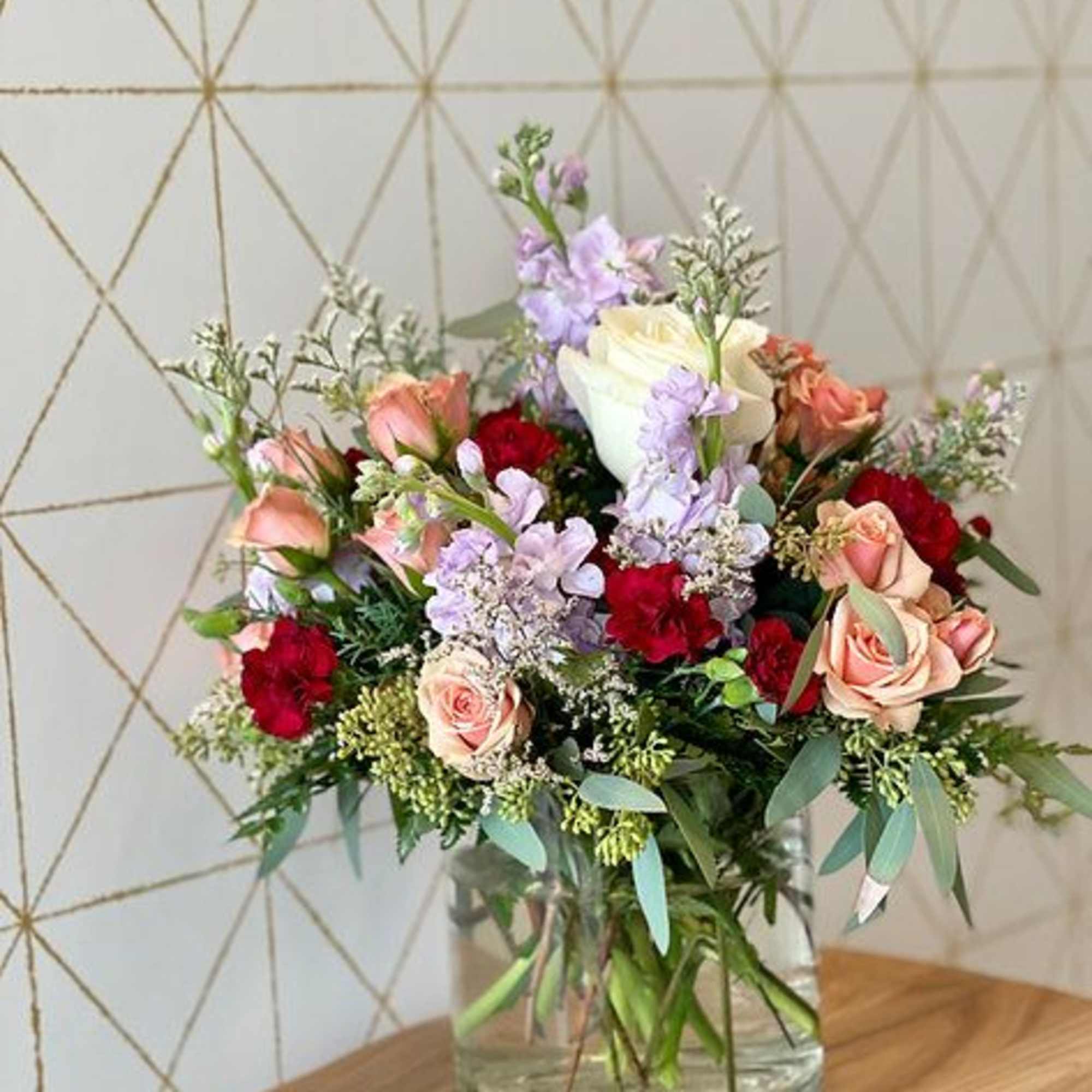 Mixed bouquet of roses, lilies, and purple blooms in a glass vase