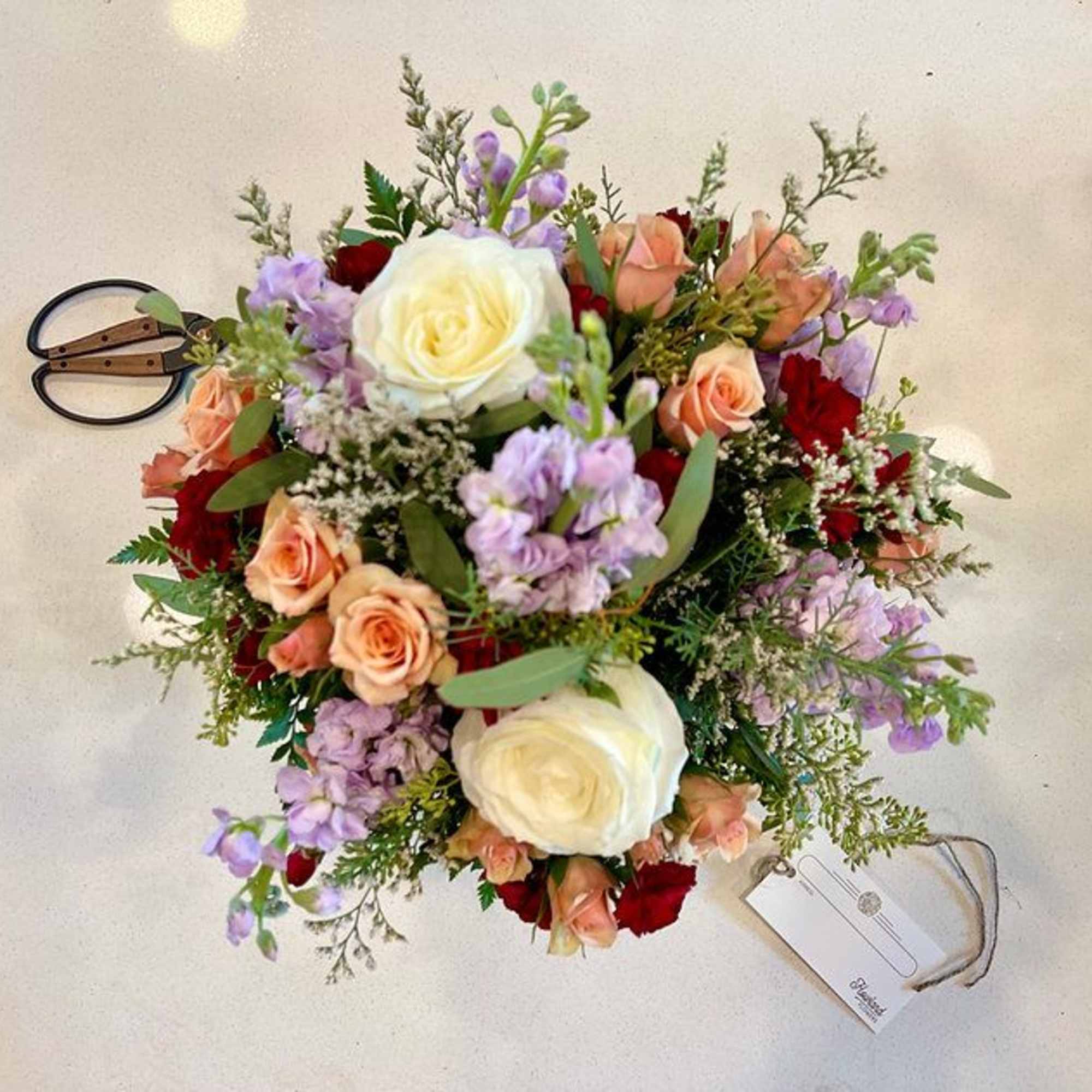 Bouquet of white, peach, red, and lavender flowers with a tag