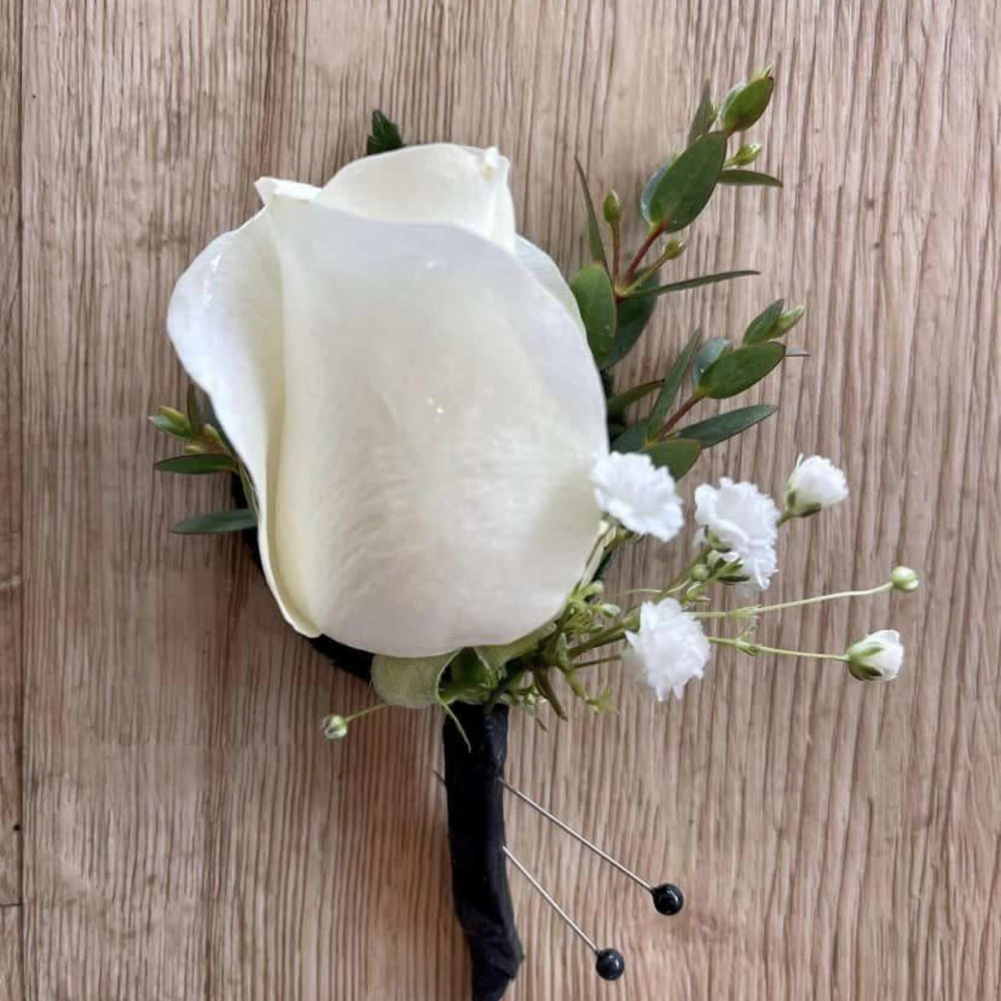 White rose boutonniere with small white filler flowers and greenery