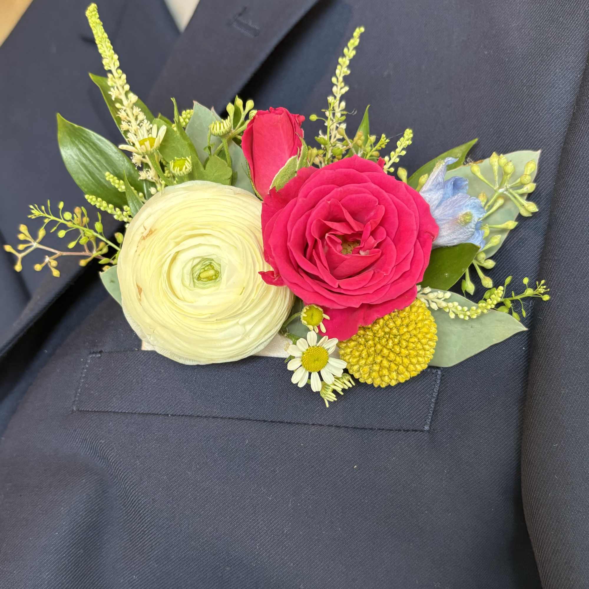 Boutonniere with pink rose, cream ranunculus, and small accent flowers