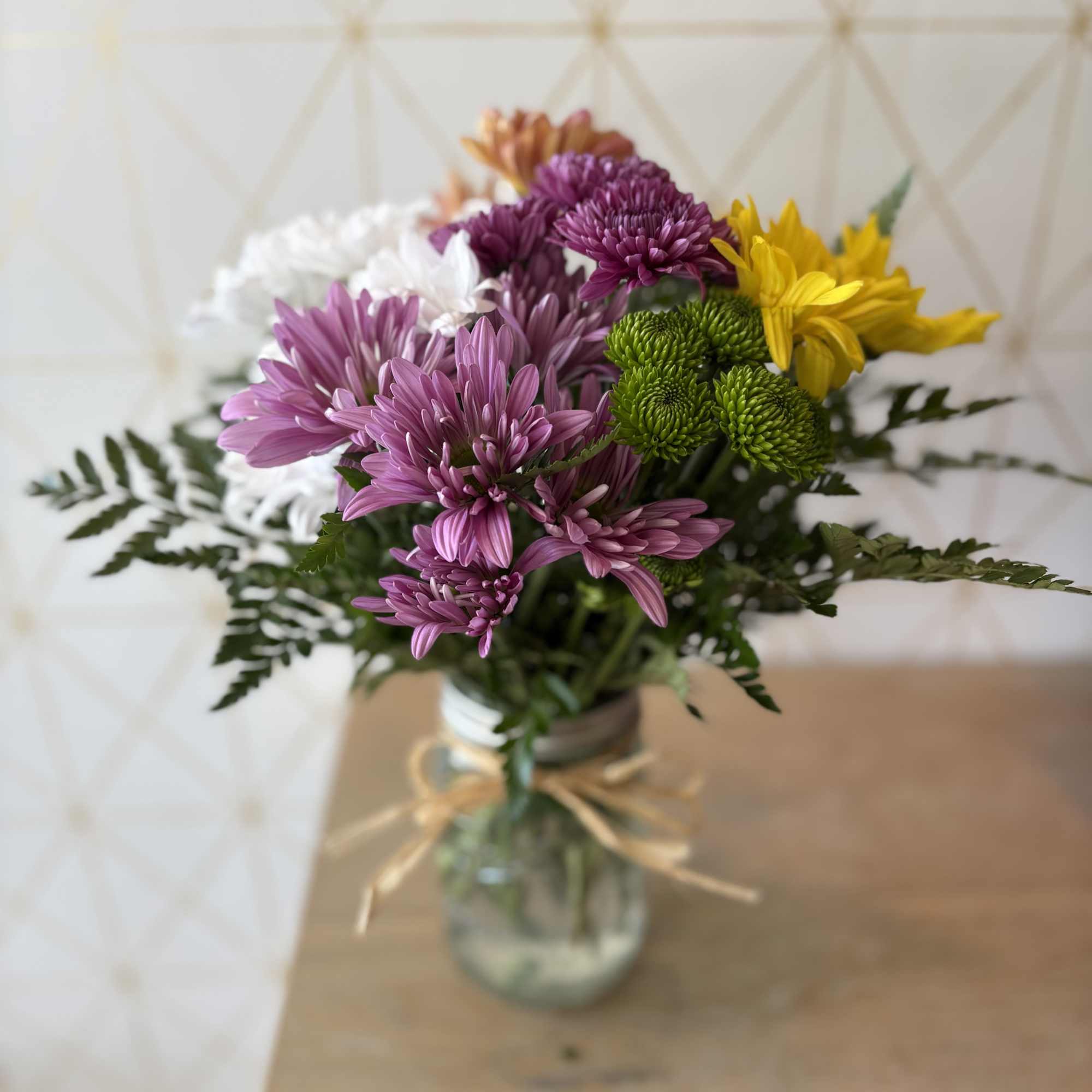 Mixed chrysanthemums in a glass jar vase with a ribbon