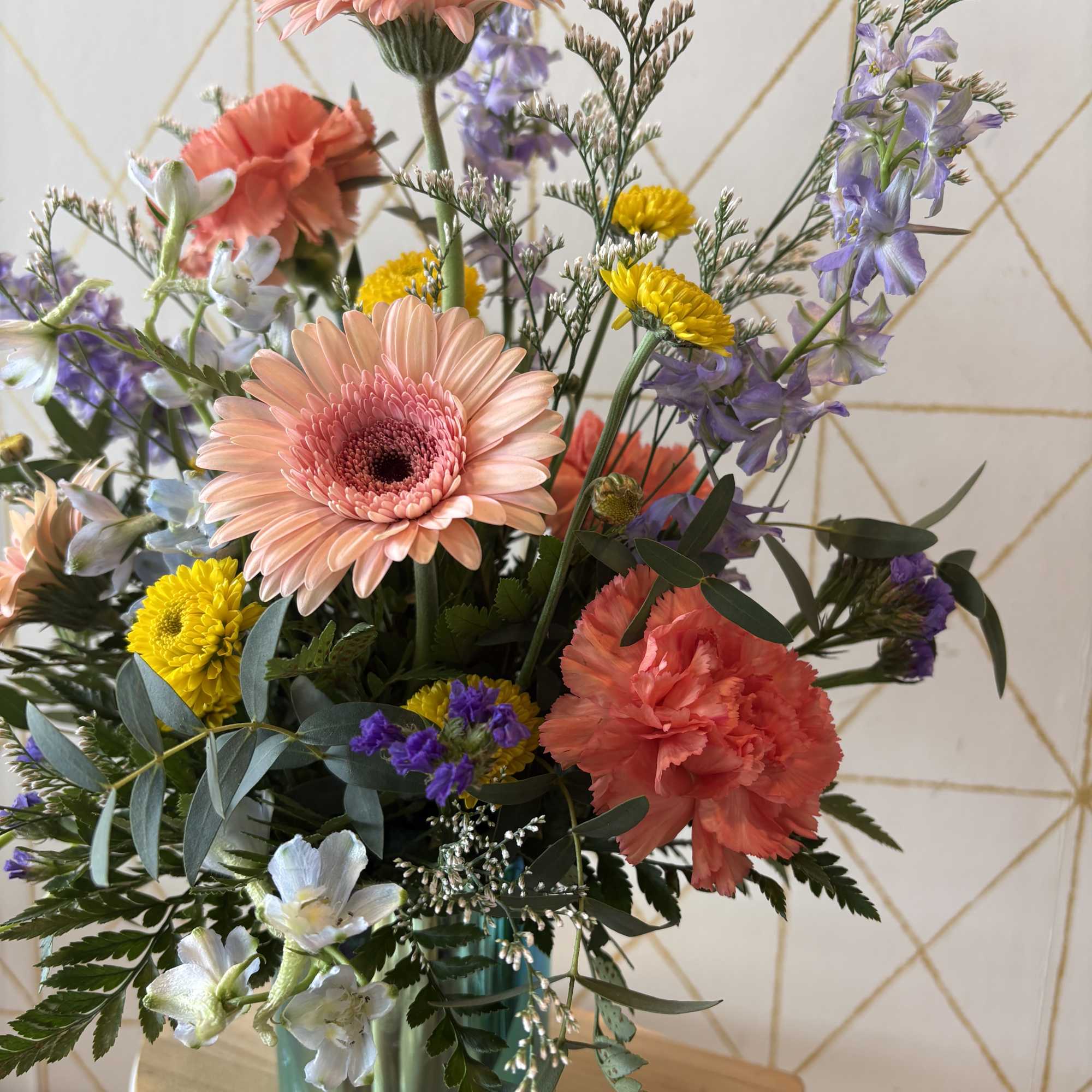 Mixed bouquet with pink gerbera daisies, coral carnations, and purple flowers in a glass vase