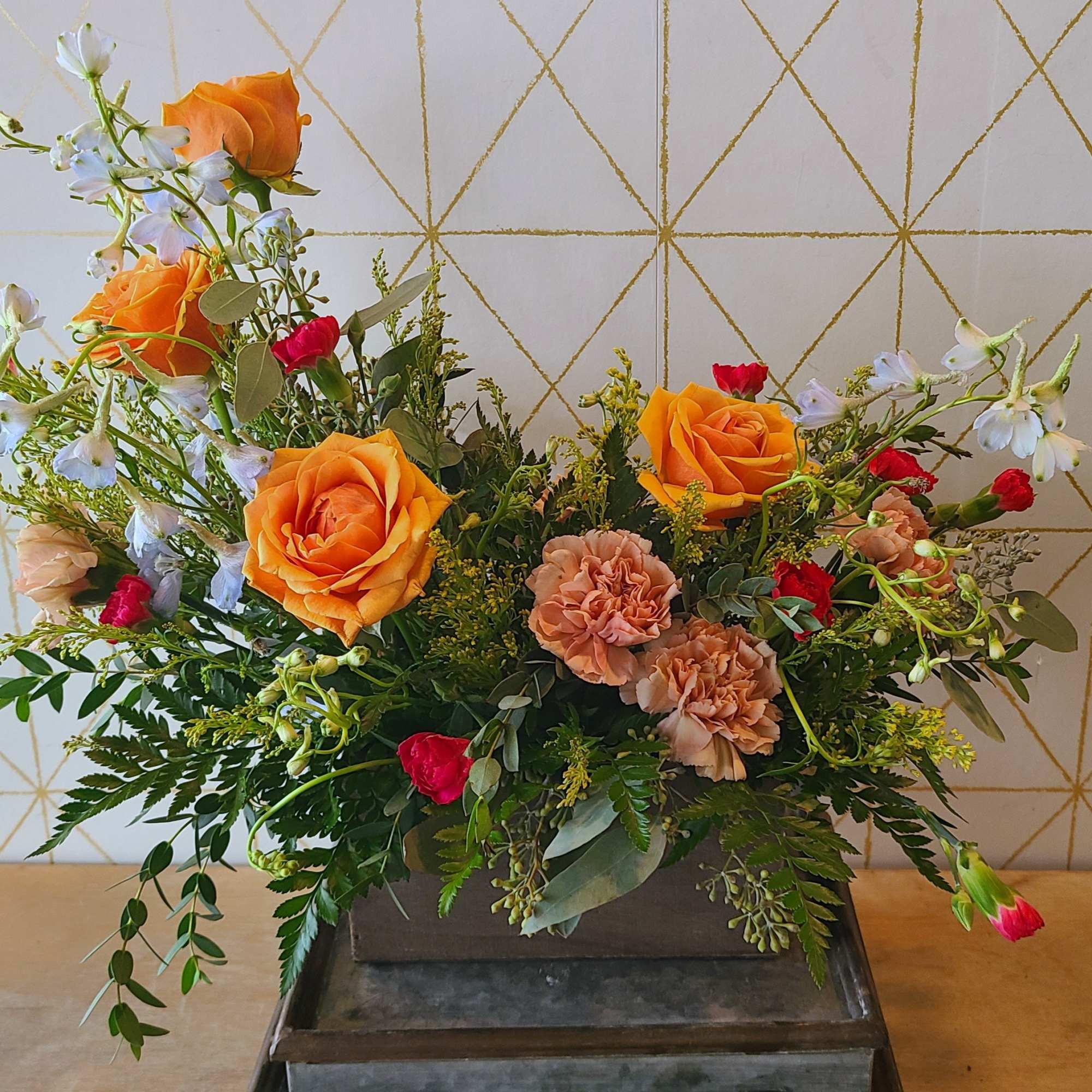 Mixed bouquet with orange roses, peach carnations, and white blossoms in a rectangular container