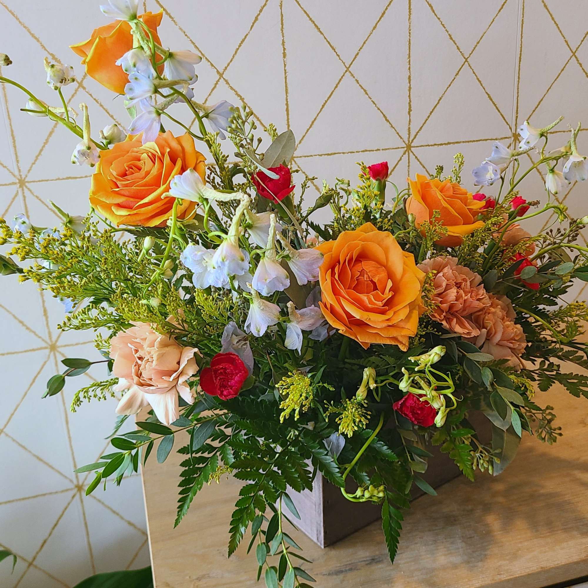 Mixed bouquet with orange roses, red carnations, and pale blue flowers in a box