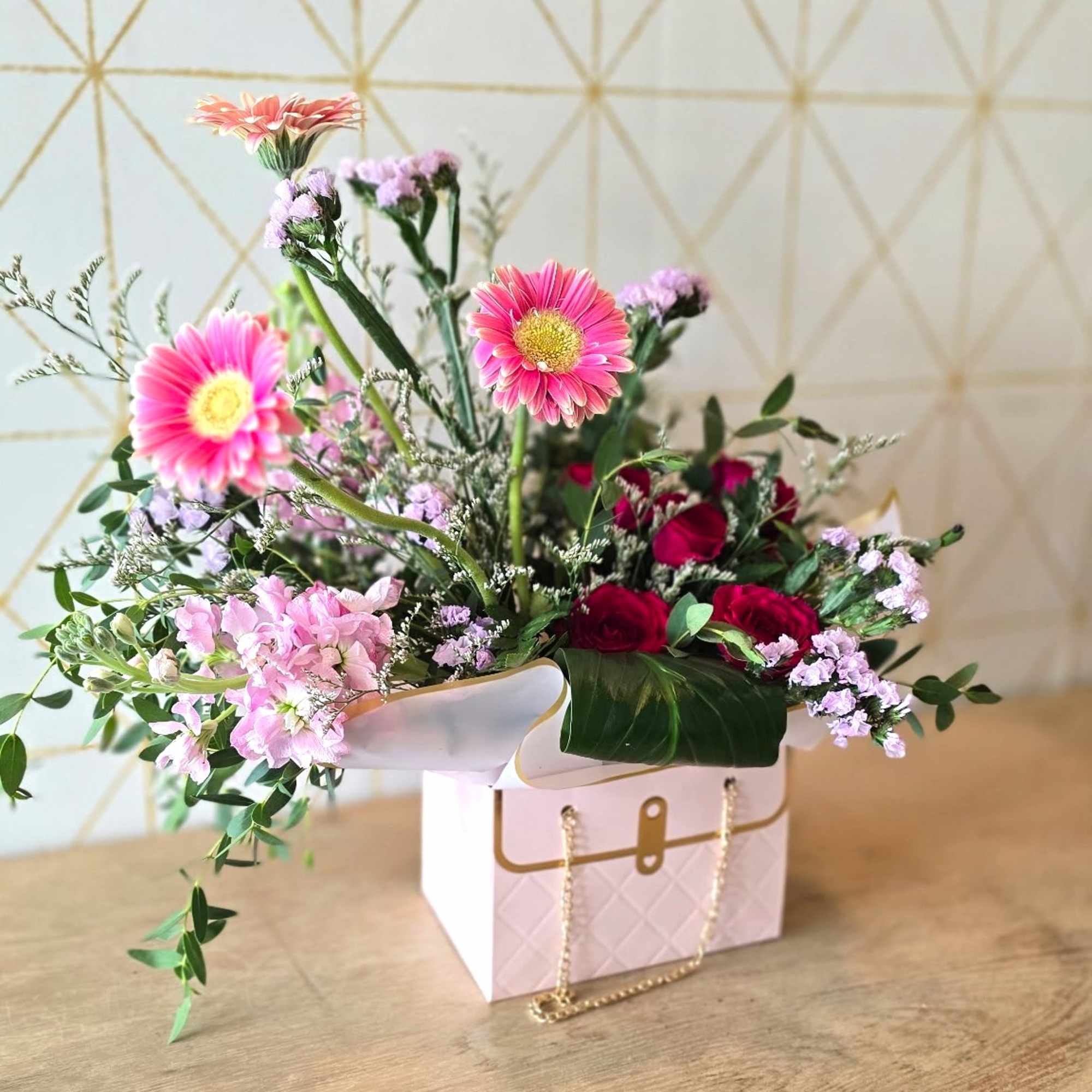 Pink and red mixed flower arrangement in a white gift box with a gold chain handle