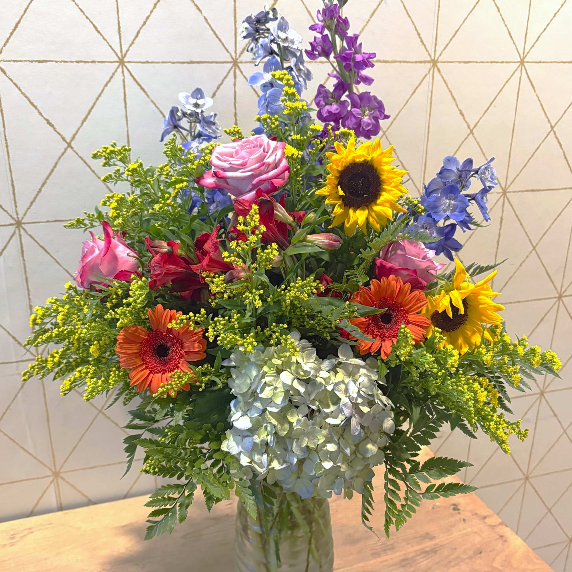 Mixed bouquet in a glass vase with roses, sunflowers, hydrangea, and blue-purple blooms