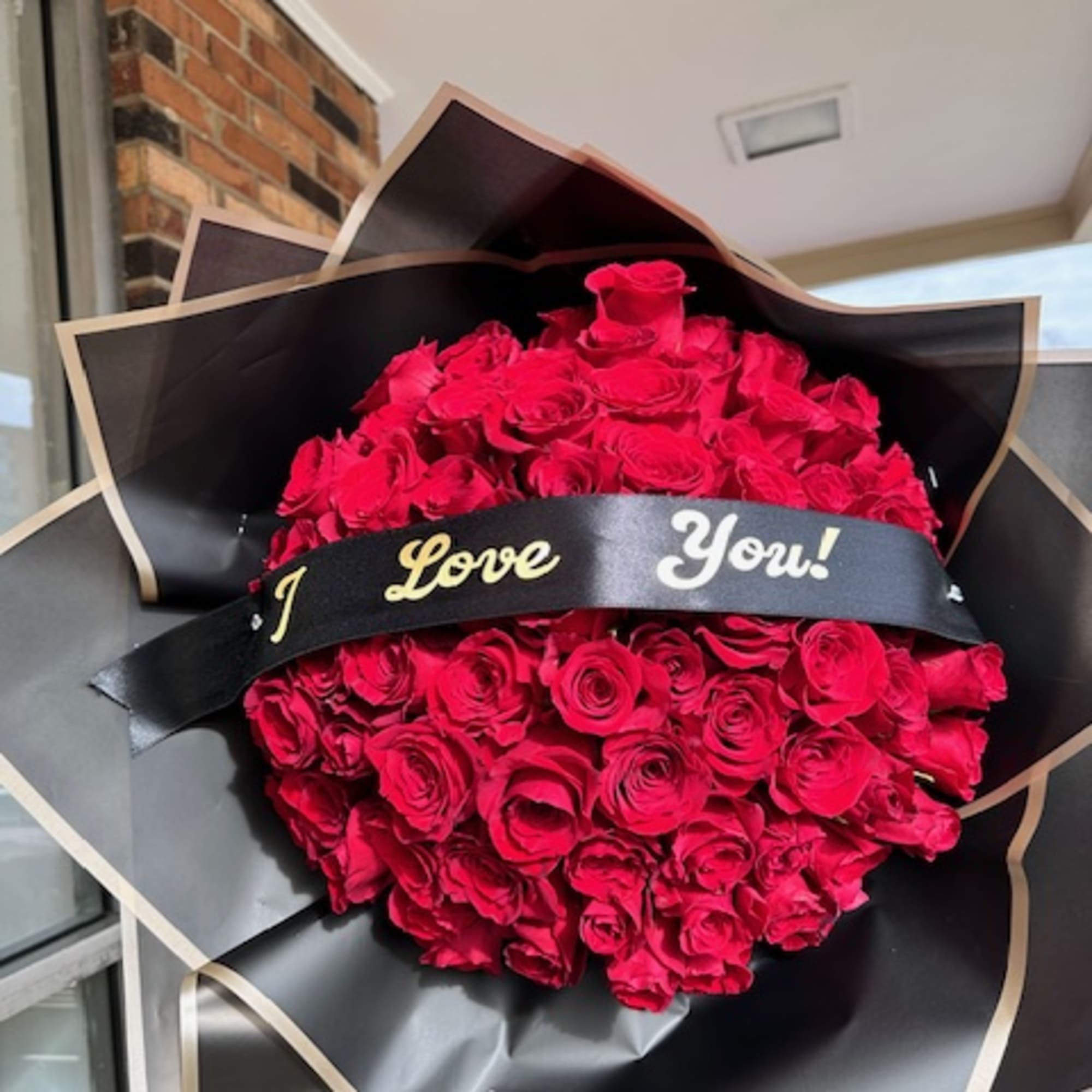 Large bouquet of red roses wrapped in black paper with a "I Love You!" ribbon