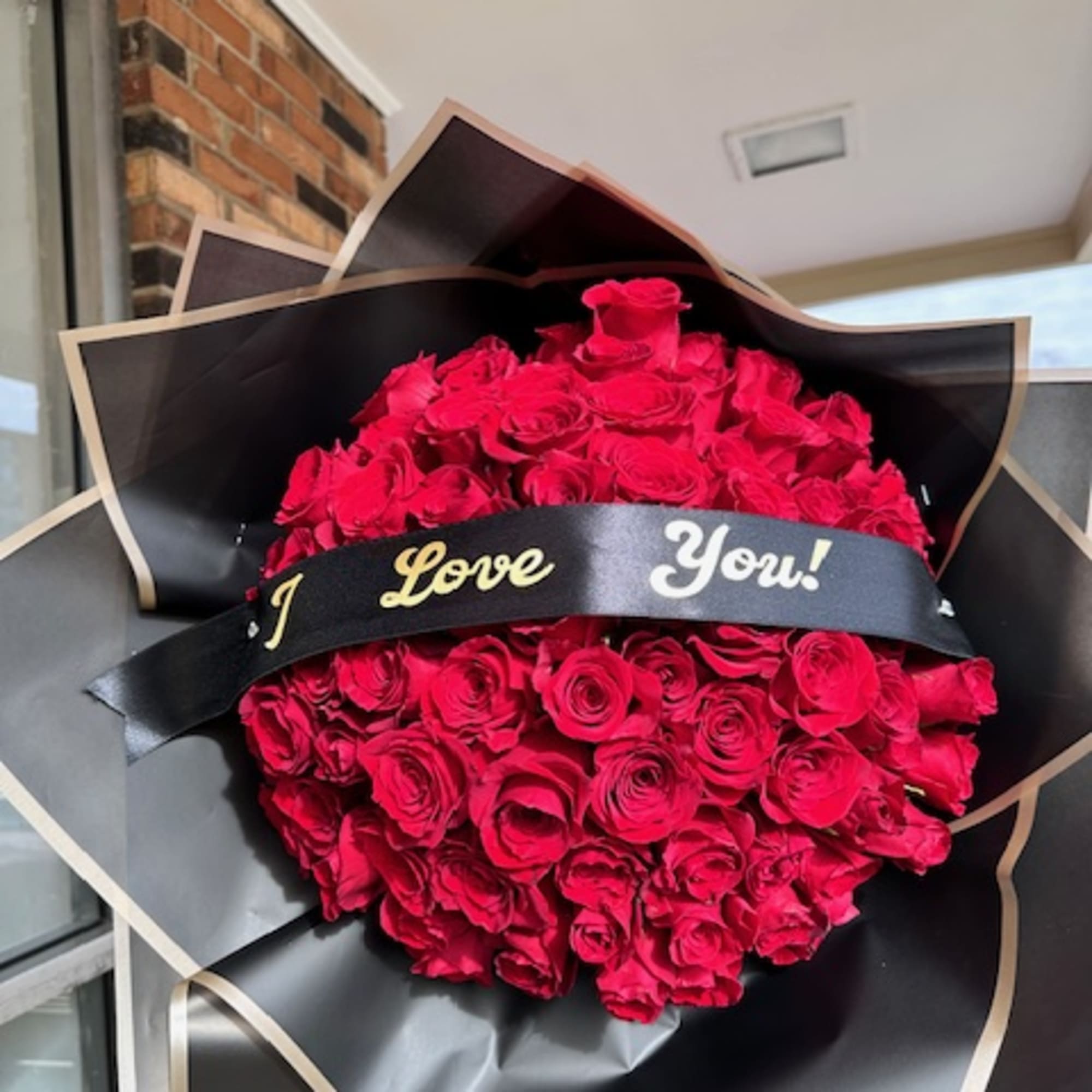 Large bouquet of red roses wrapped in black paper with a ribbon reading "I Love You!"