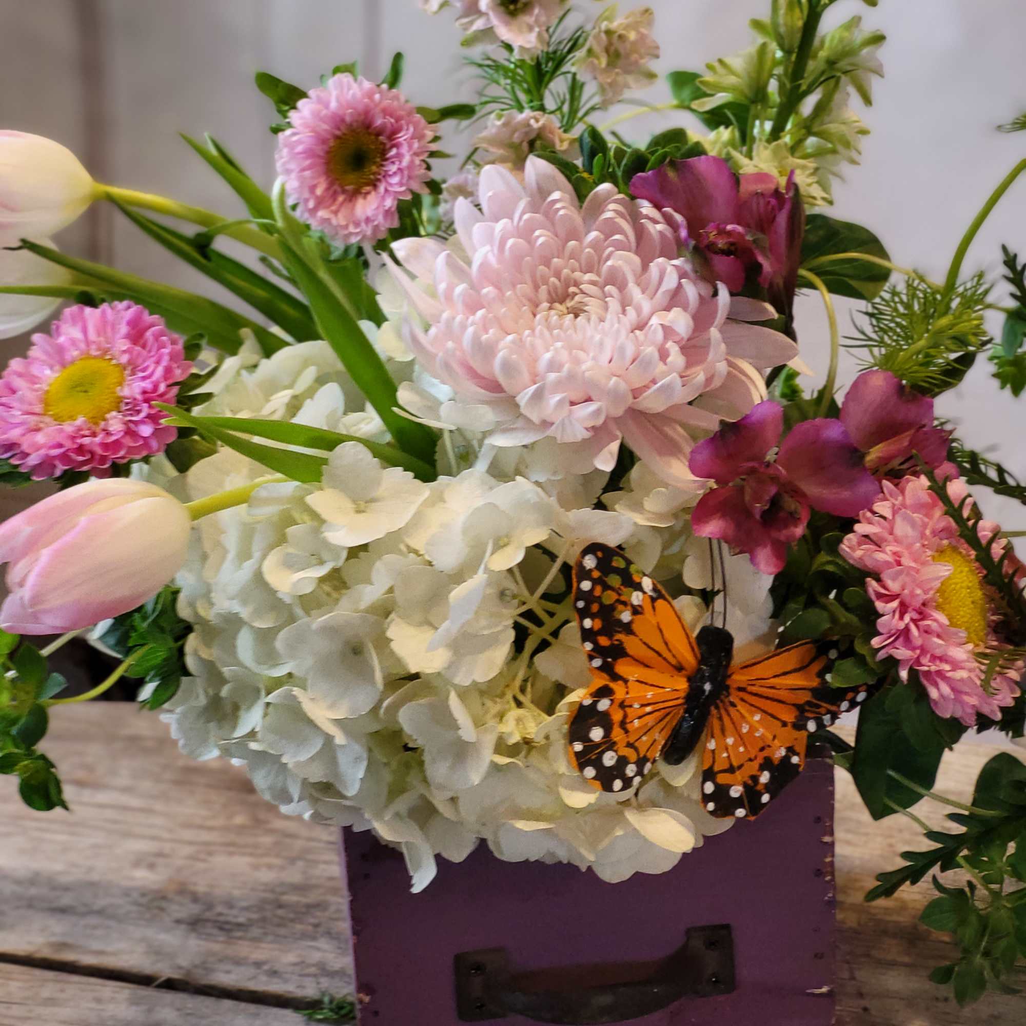 Mixed pink and white flowers in a purple box with a butterfly accent