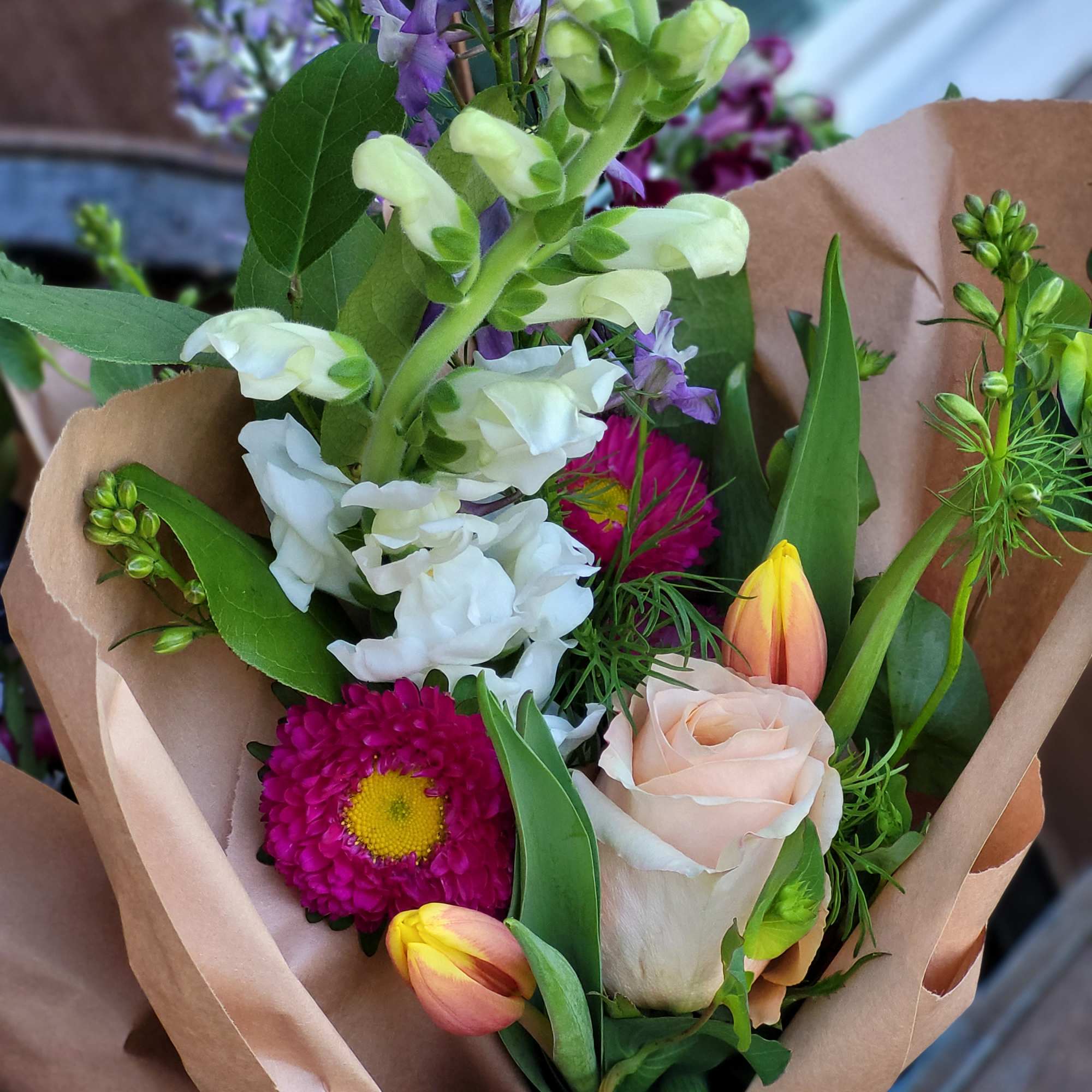 Mixed bouquet with a peach rose, tulips, and purple blooms in brown paper