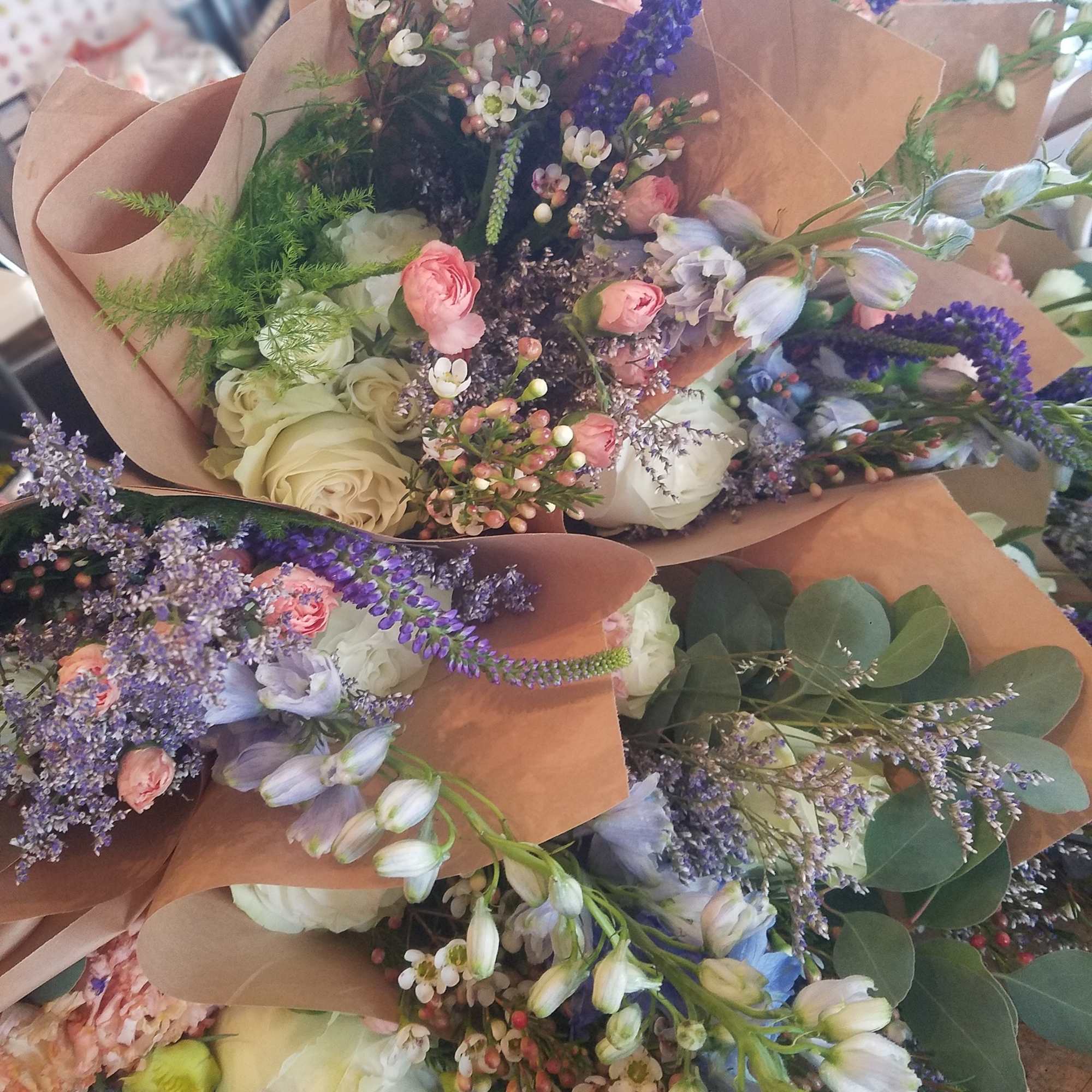 Several mixed bouquets with roses, purple flowers, and brown paper wrapping.