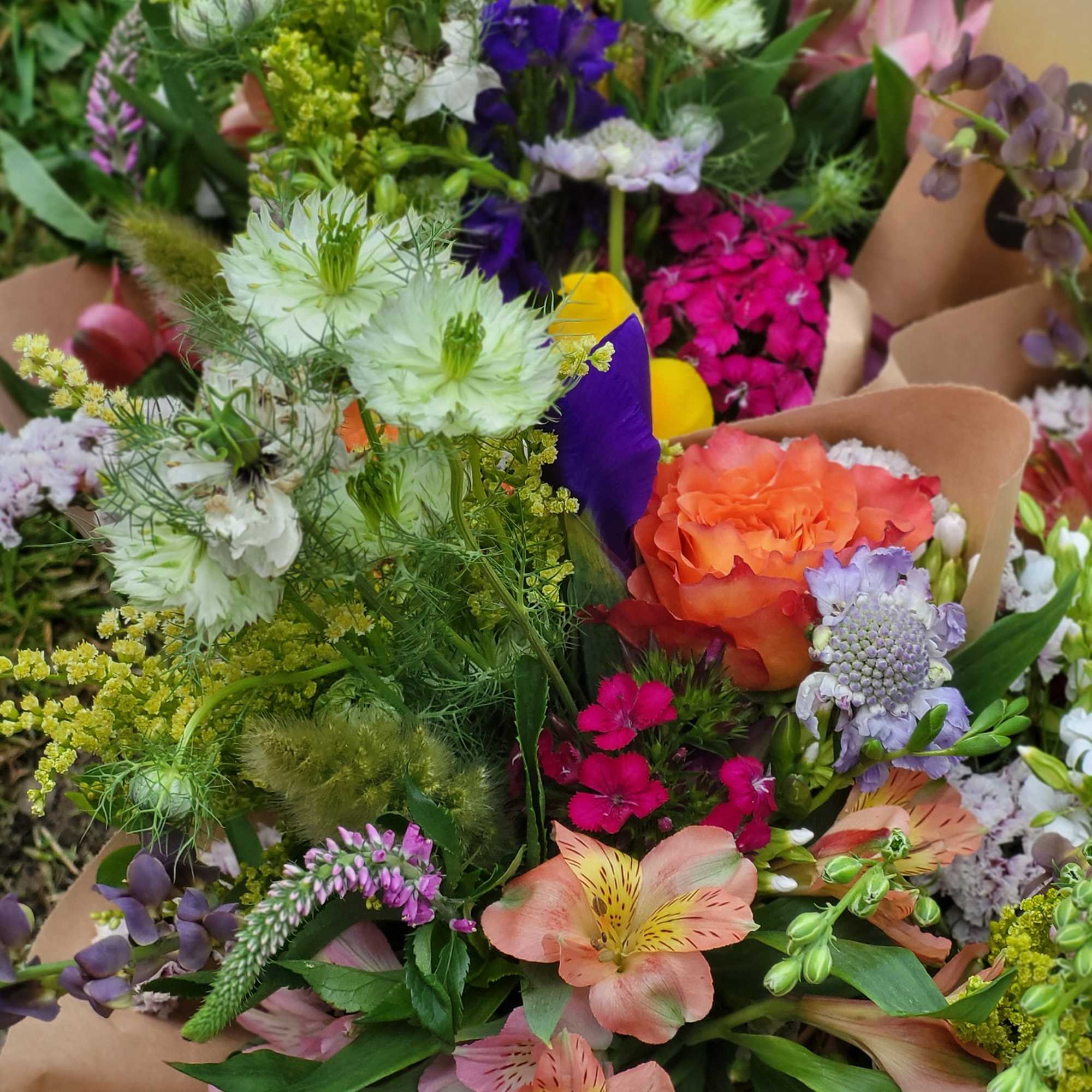 Mixed bouquet with orange, pink, purple, and white flowers wrapped in kraft paper