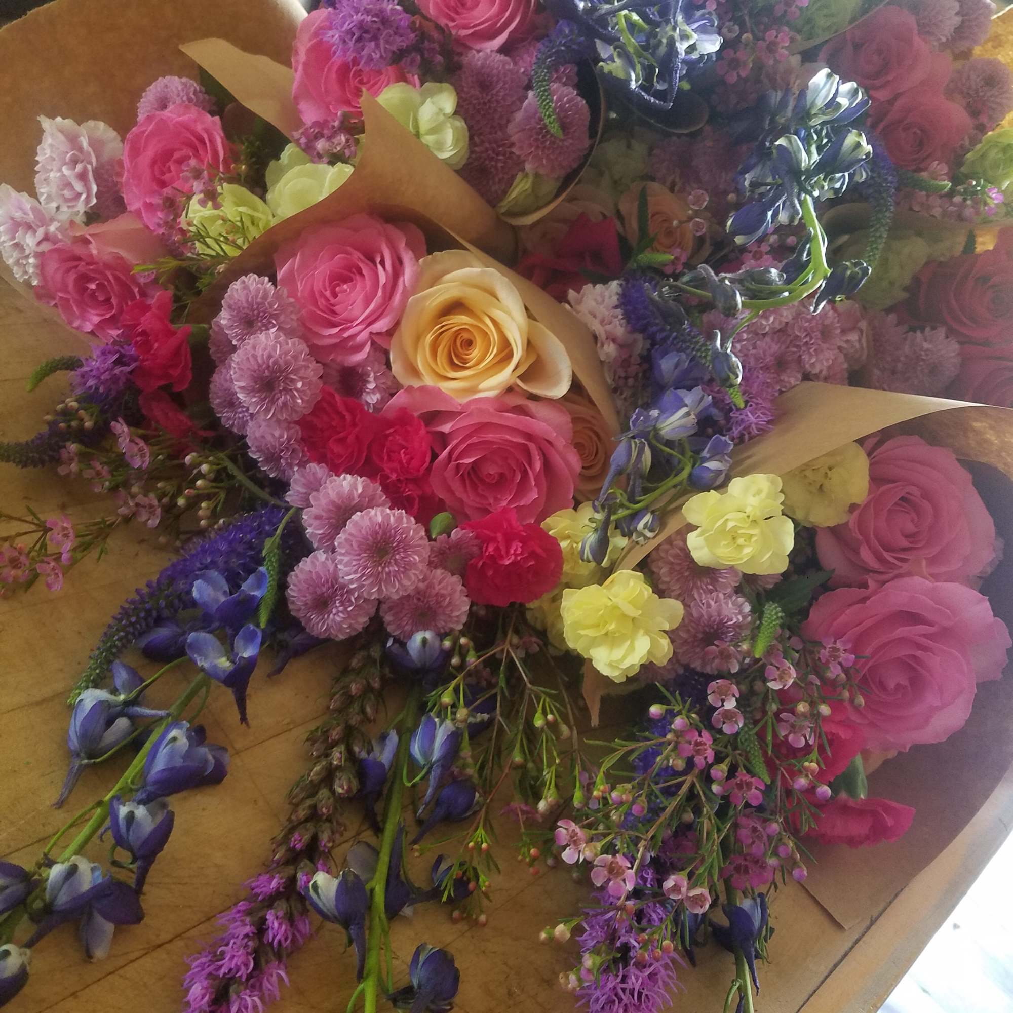 Bouquets of pink, purple, yellow, and blue flowers wrapped in brown paper