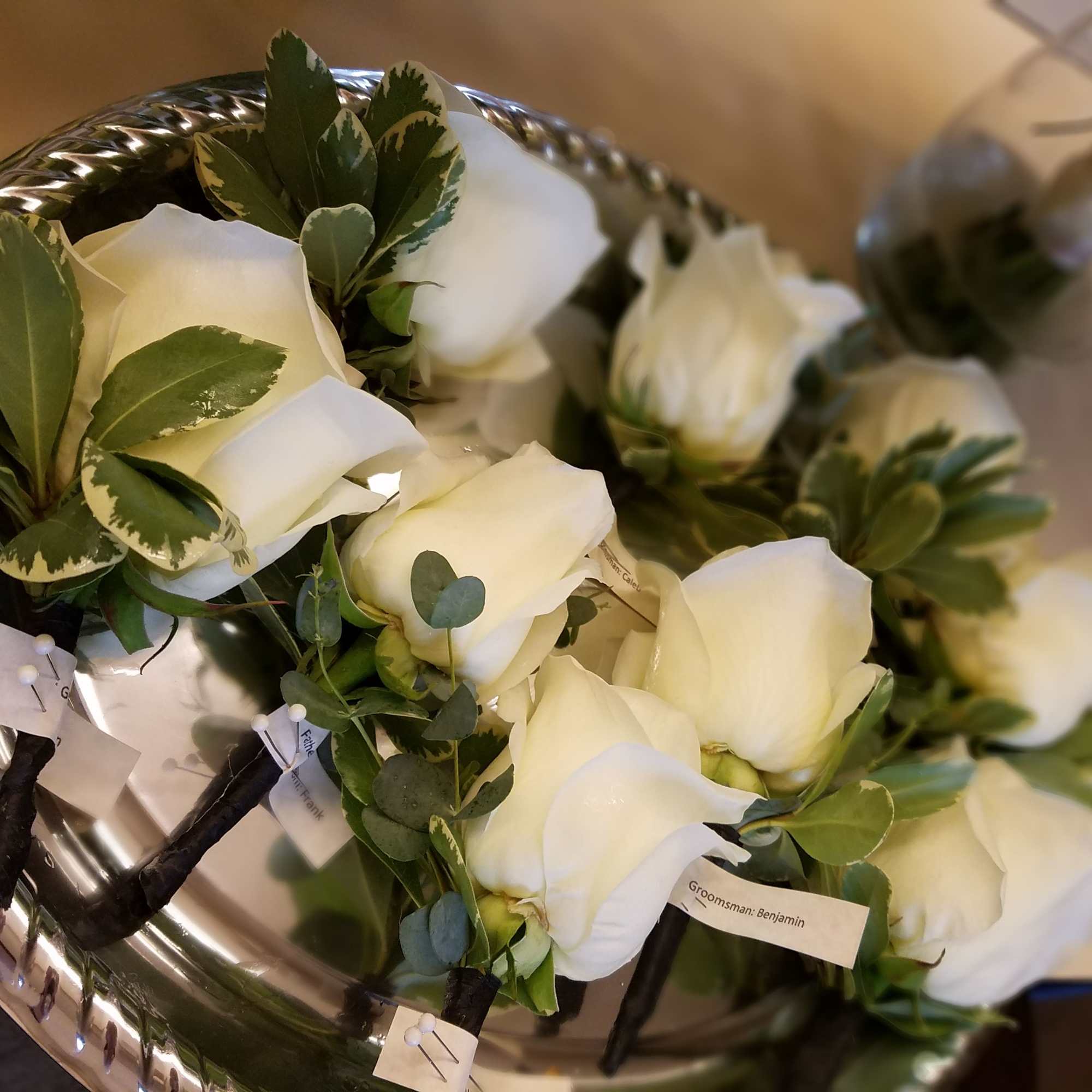 White rose boutonnieres with greenery on a silver tray