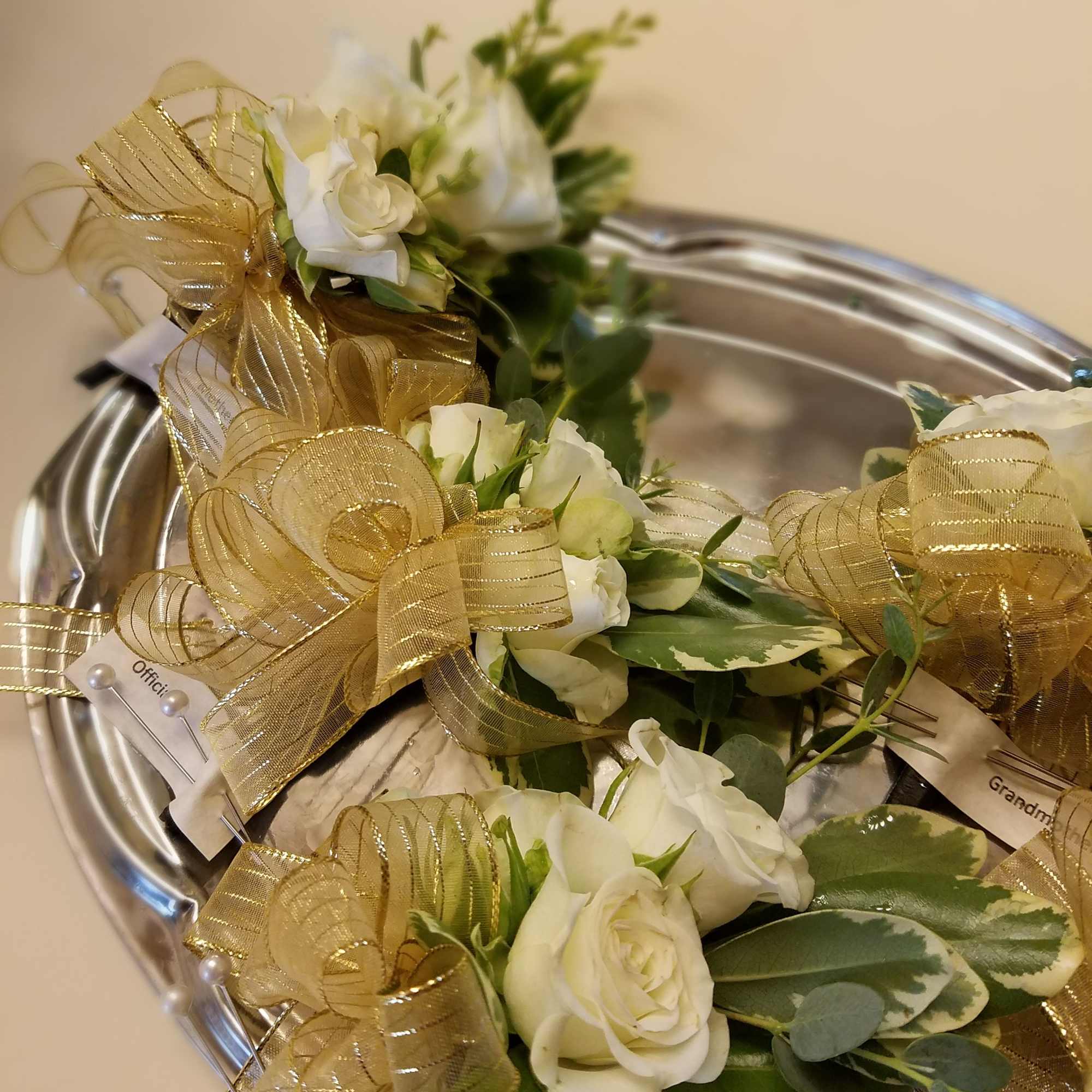 White rose corsages with gold ribbon on a silver tray